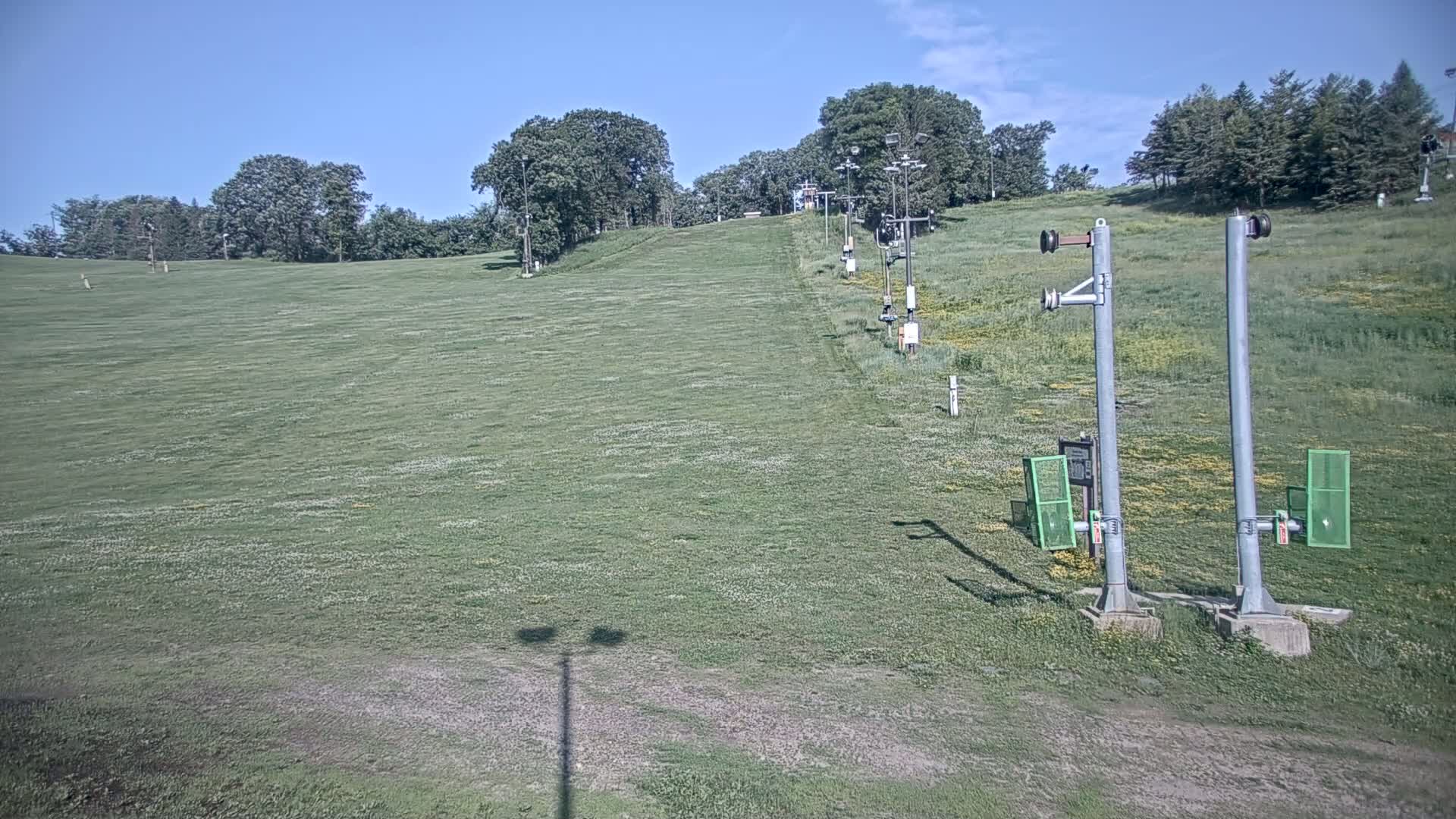 A grassy ski slope with a chairlift in the background on a clear, sunny day.