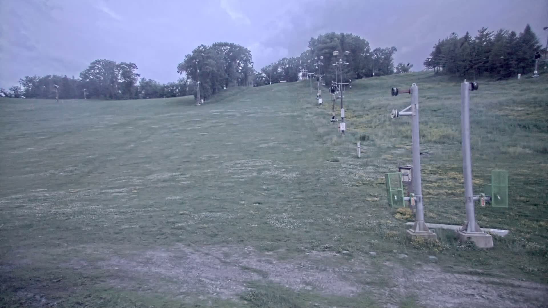 A grassy ski slope with a chairlift extending uphill under an overcast sky.