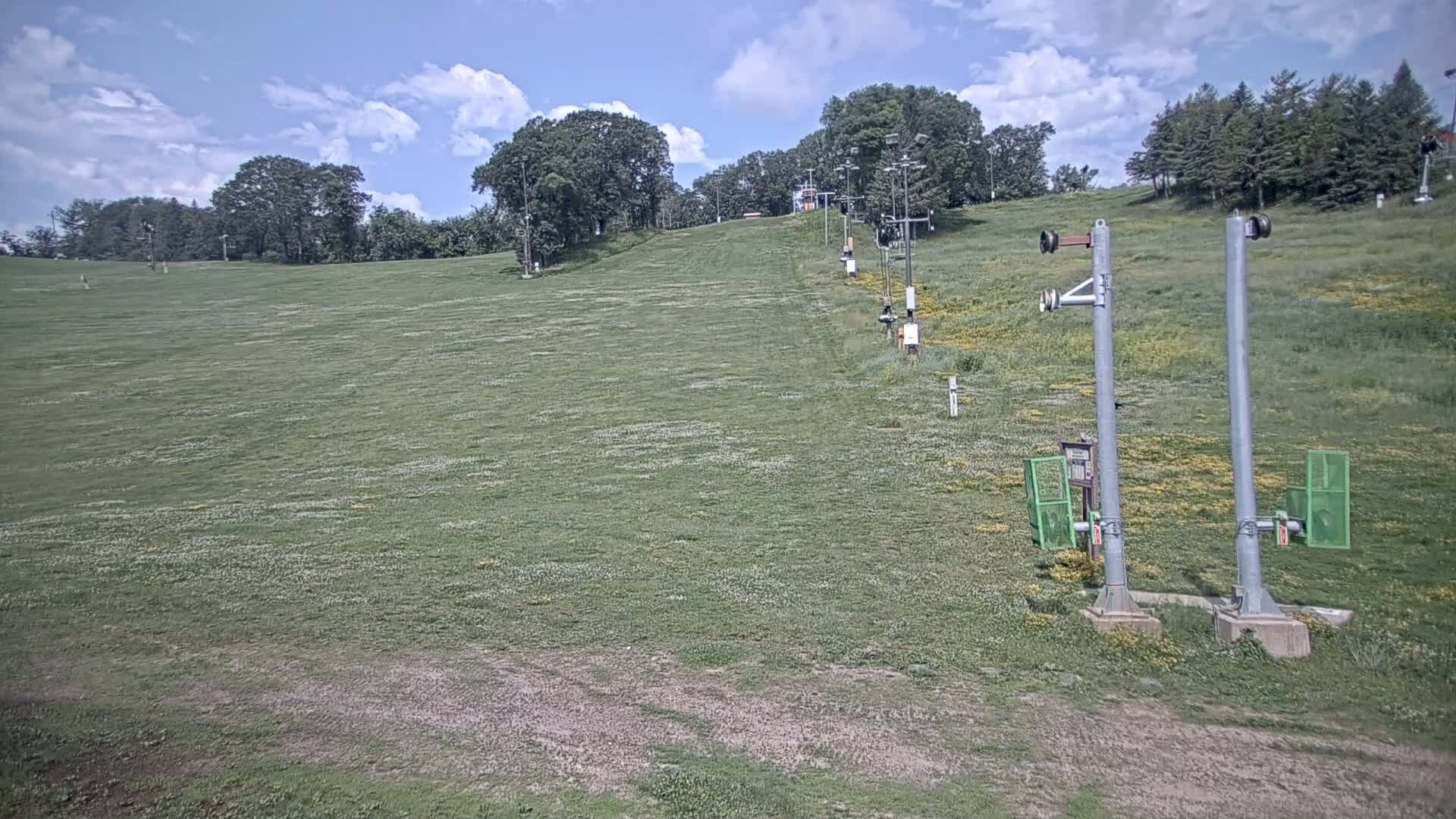 A grassy hill with a chairlift and trees in the background under a partly cloudy sky.