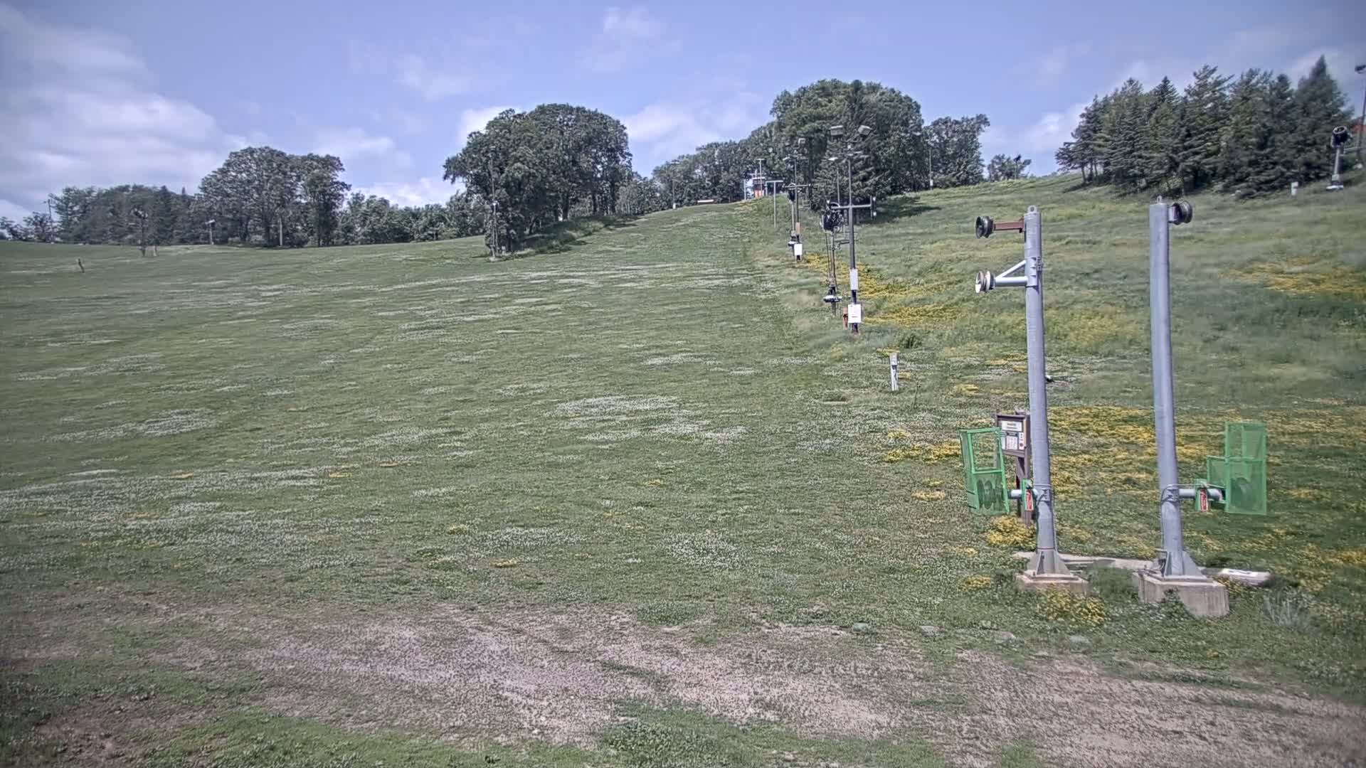 A grassy ski slope with a chairlift in the background under a partly cloudy sky.