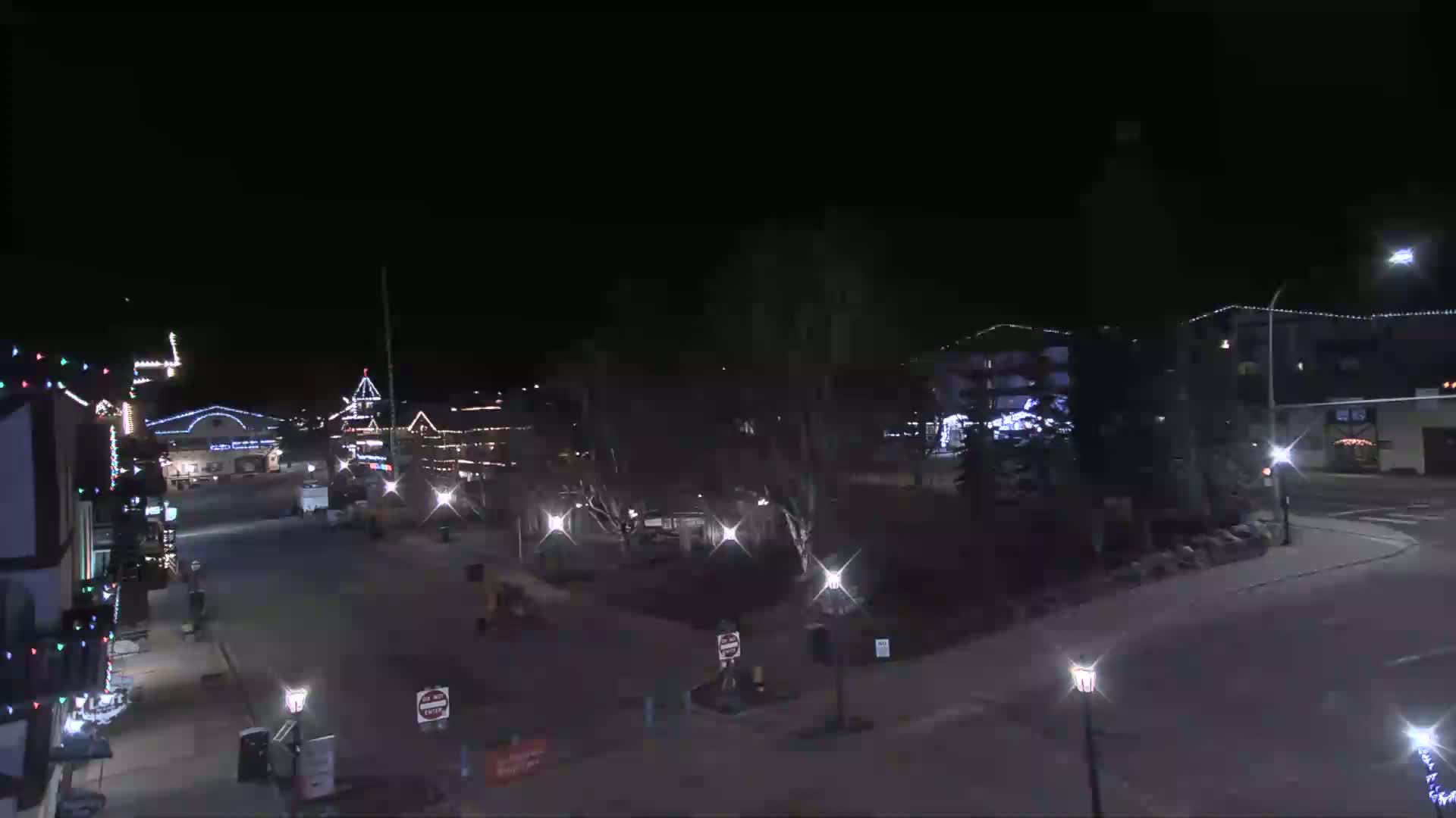A nighttime view of a town square with illuminated buildings and trees, under a clear, dark sky.