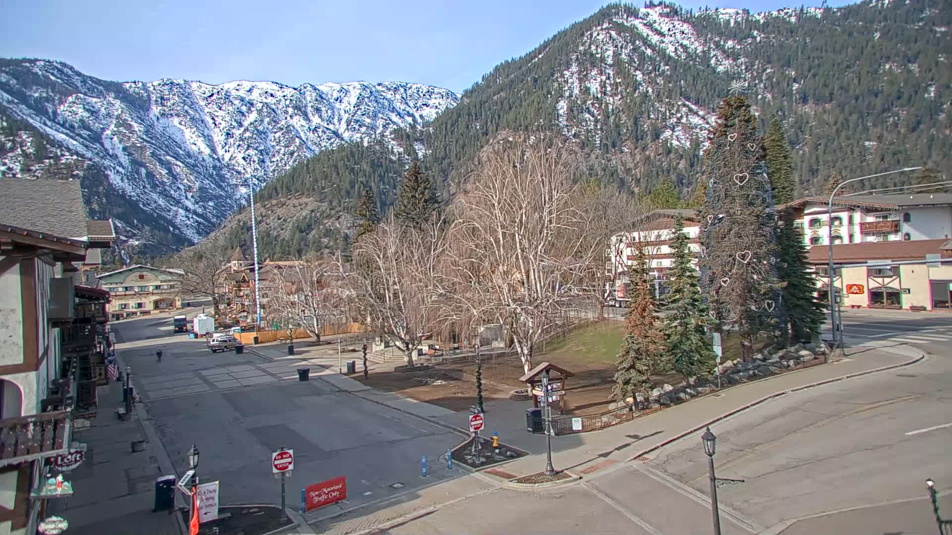 A mostly empty town square with snow-capped mountains in the background under a clear, sunny sky.