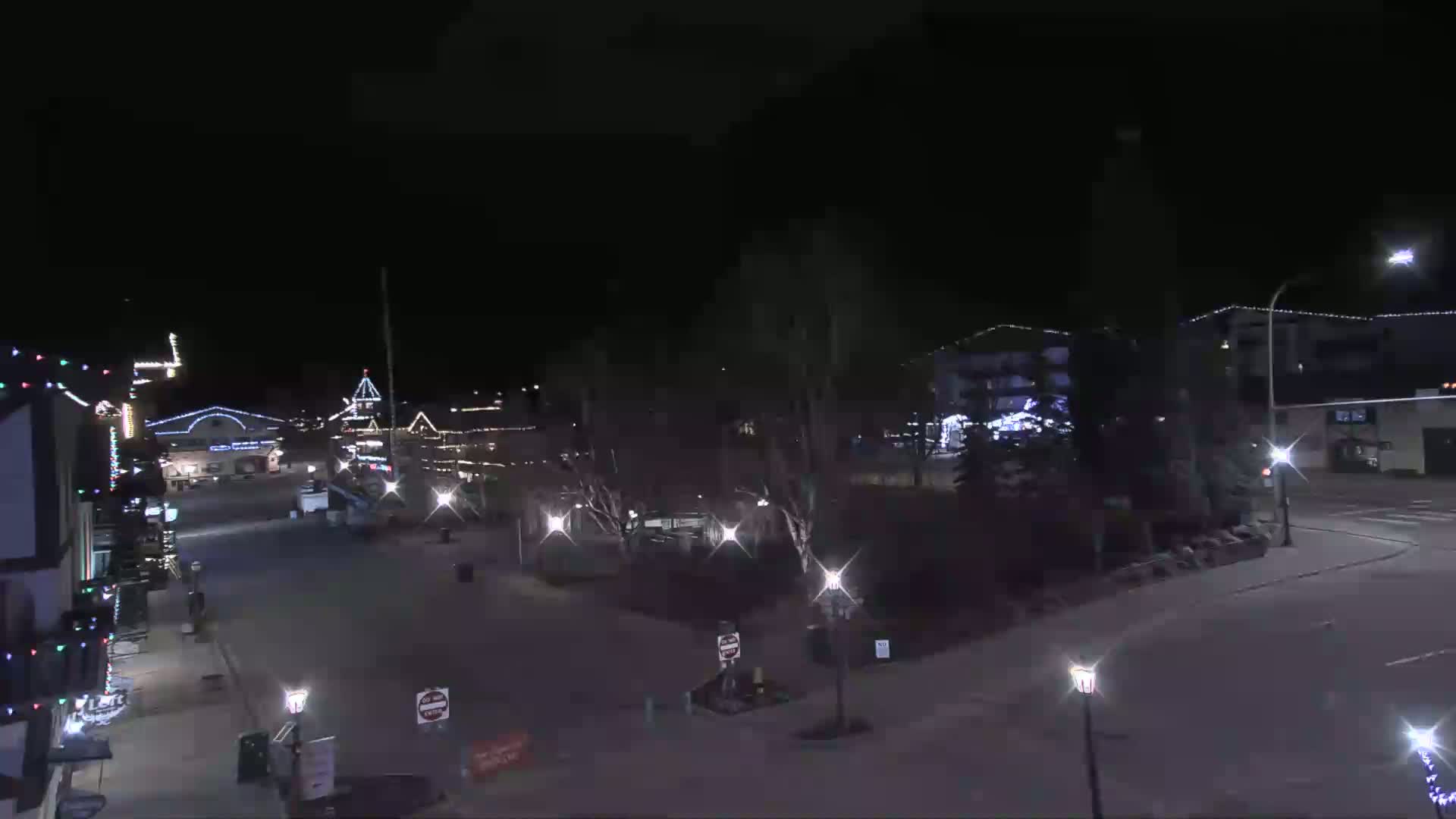 A nighttime view of a town square with buildings decorated with holiday lights, under a clear, dark sky.