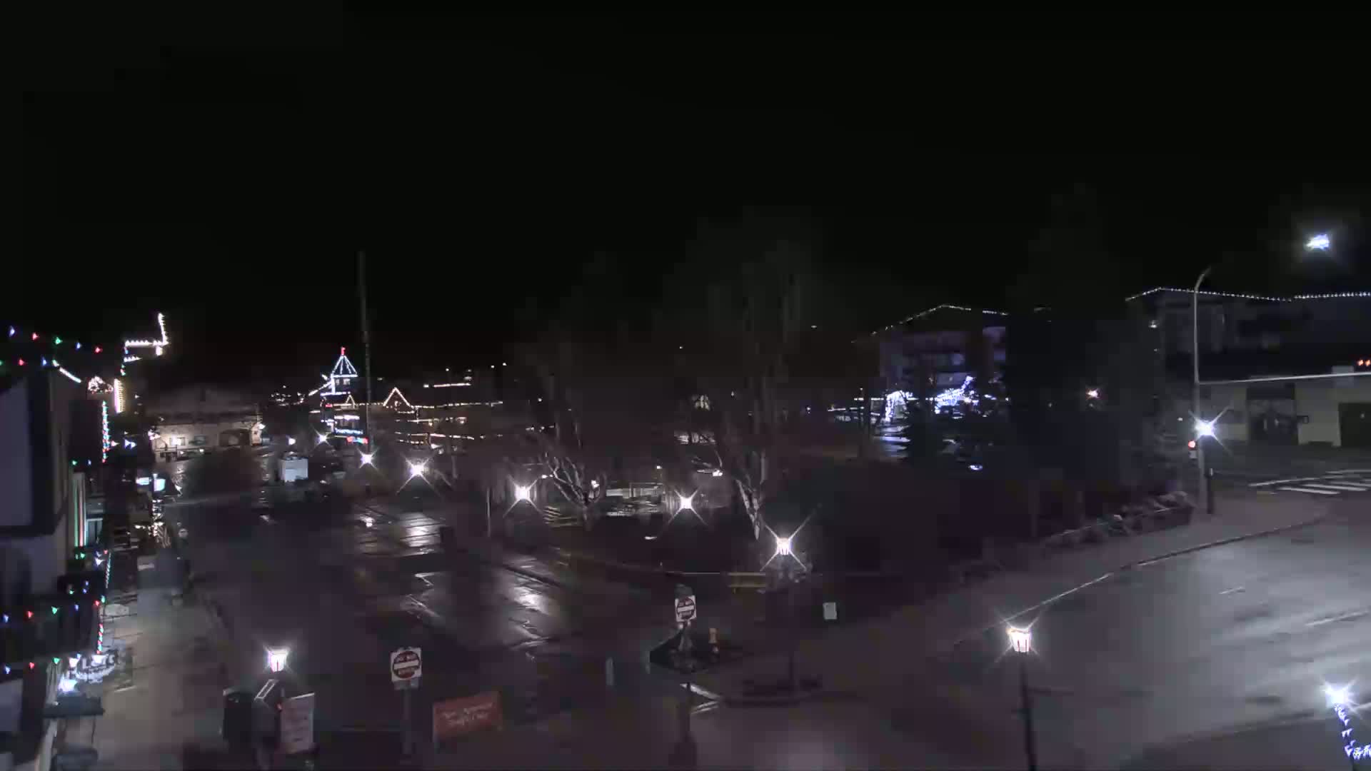 A nighttime view of a town square with some buildings decorated with lights and sparsely populated streets.