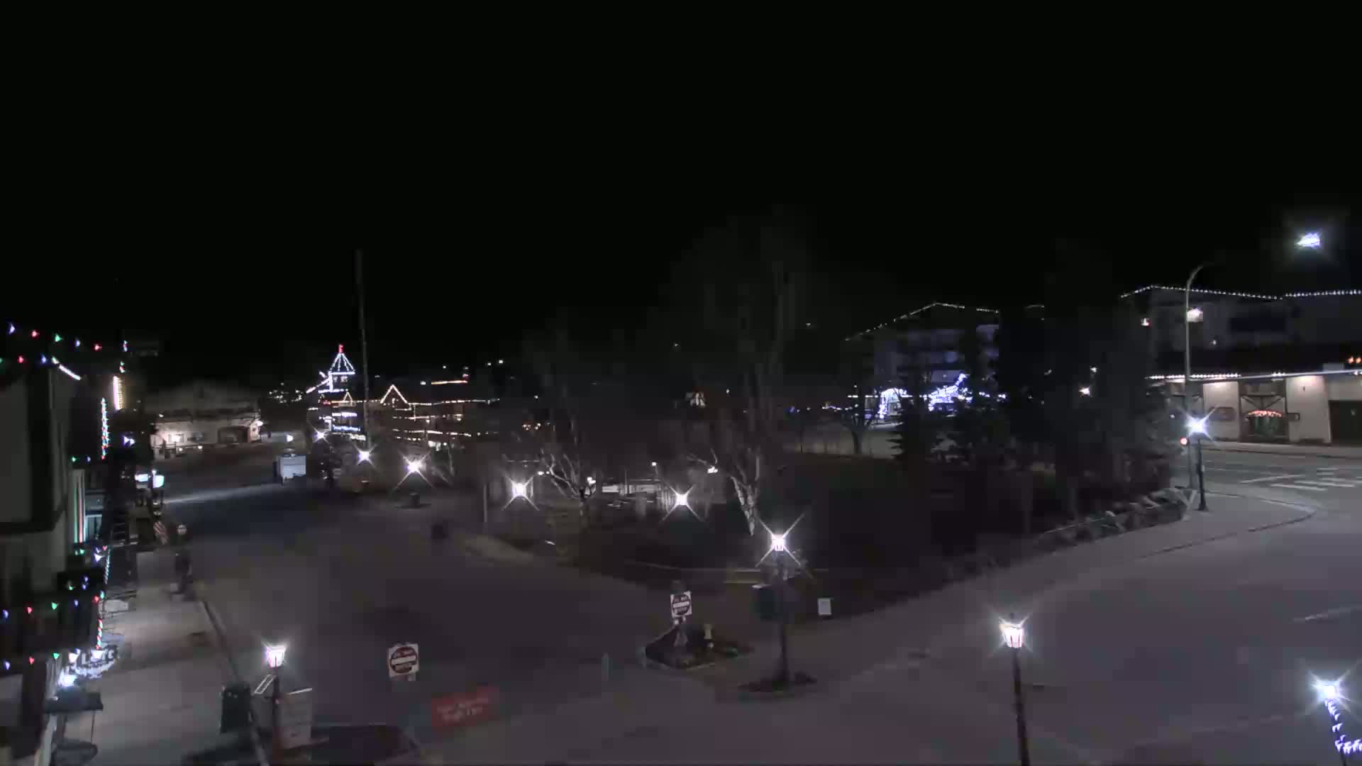 A nighttime view of a town square with buildings decorated with lights, and sparsely populated streets.