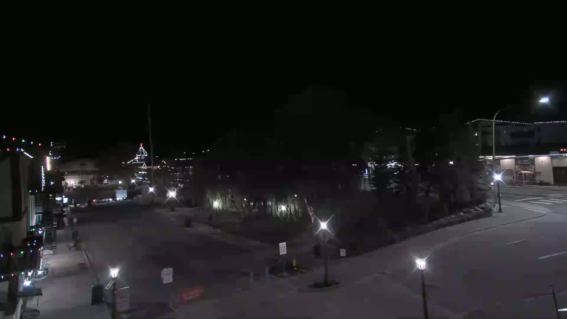 A nighttime view of a town square with several buildings decorated with Christmas lights, under a clear, dark sky.