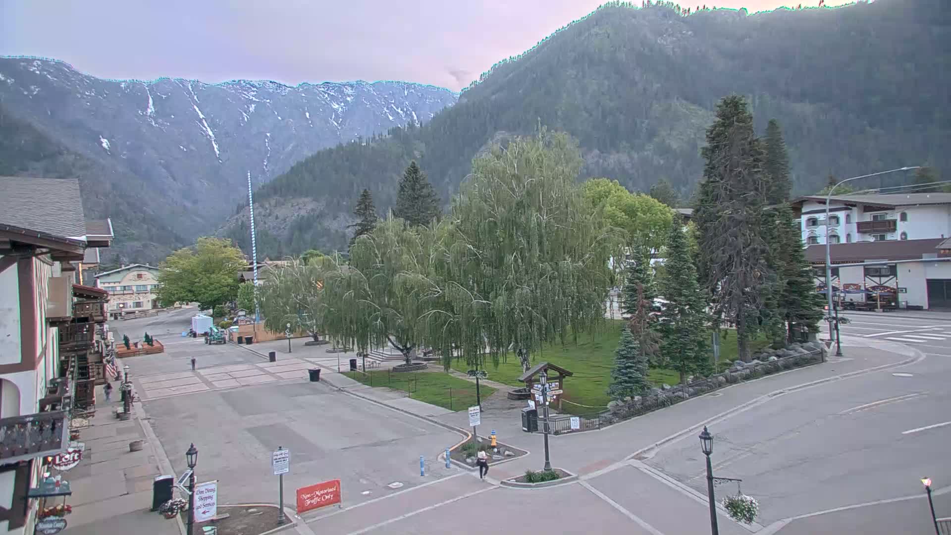A mostly empty town square sits before snow-capped mountains under an overcast sky.