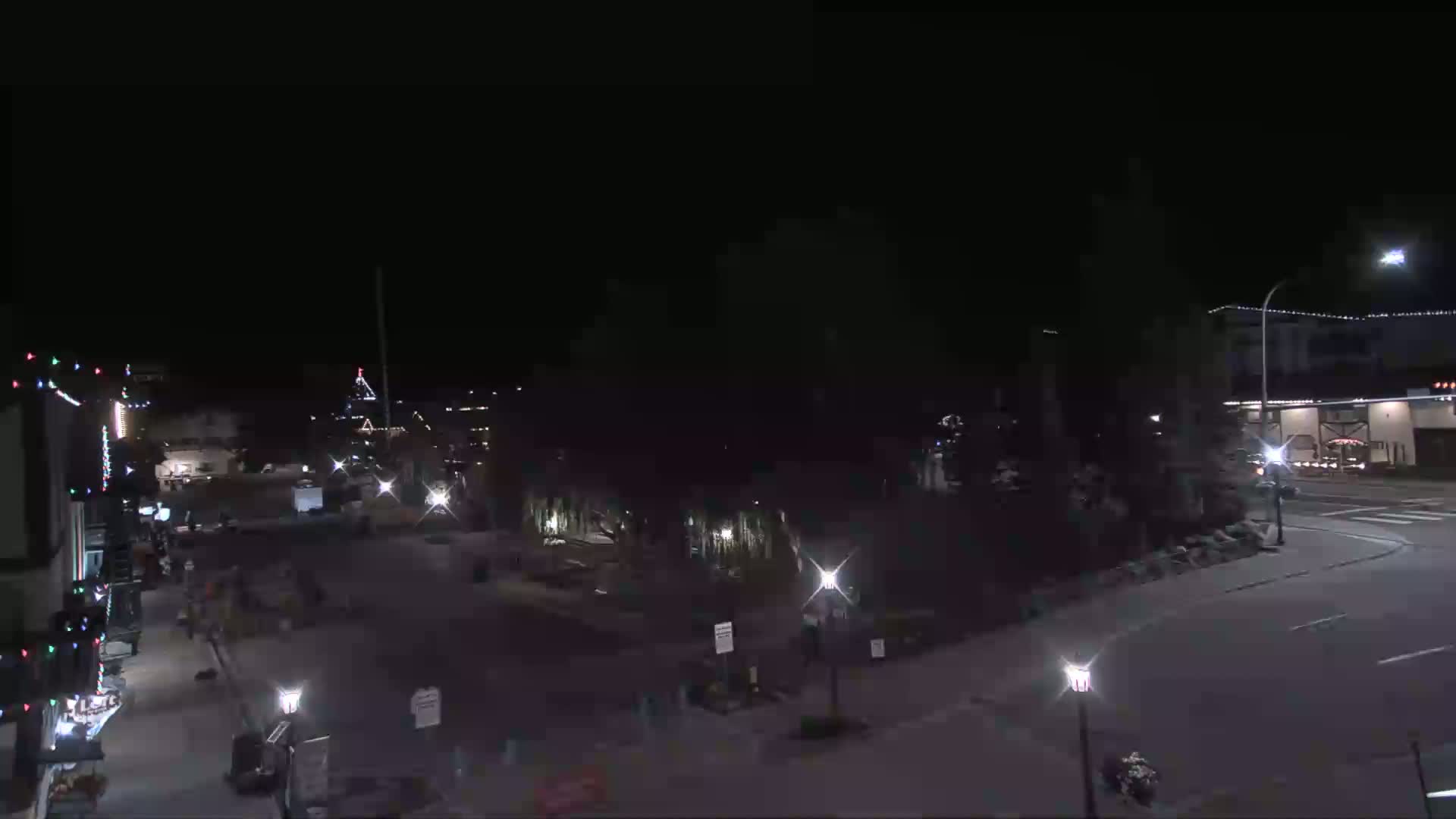 A nighttime view of a sparsely populated town square with a few streetlights illuminating the area under a clear, dark sky.