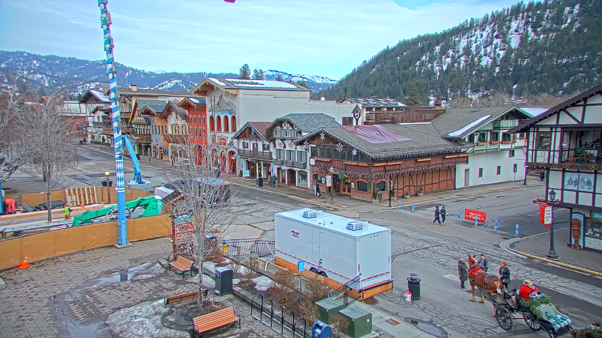 A town square with Bavarian-style buildings, a horse-drawn carriage, and a partly cloudy sky.