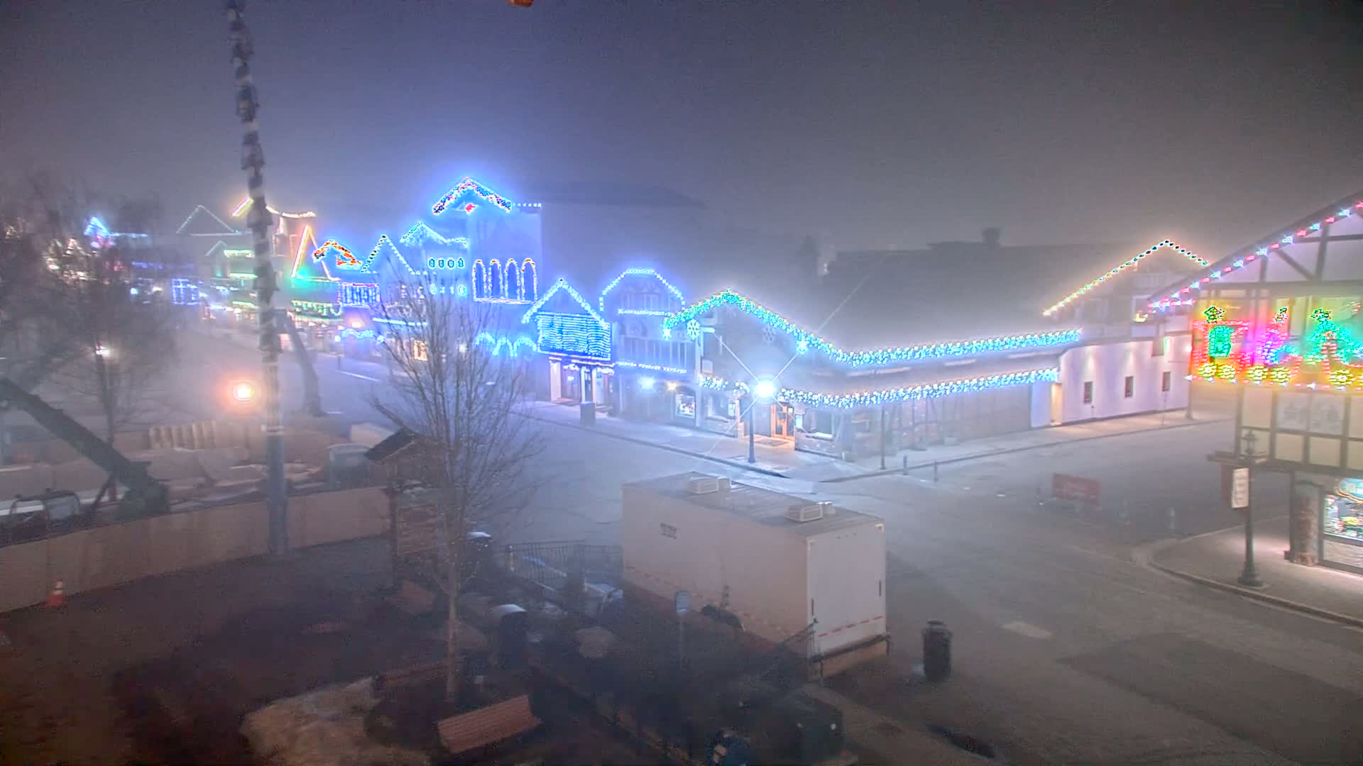 A fog-shrouded street at night, lined with buildings decorated with colorful Christmas lights.