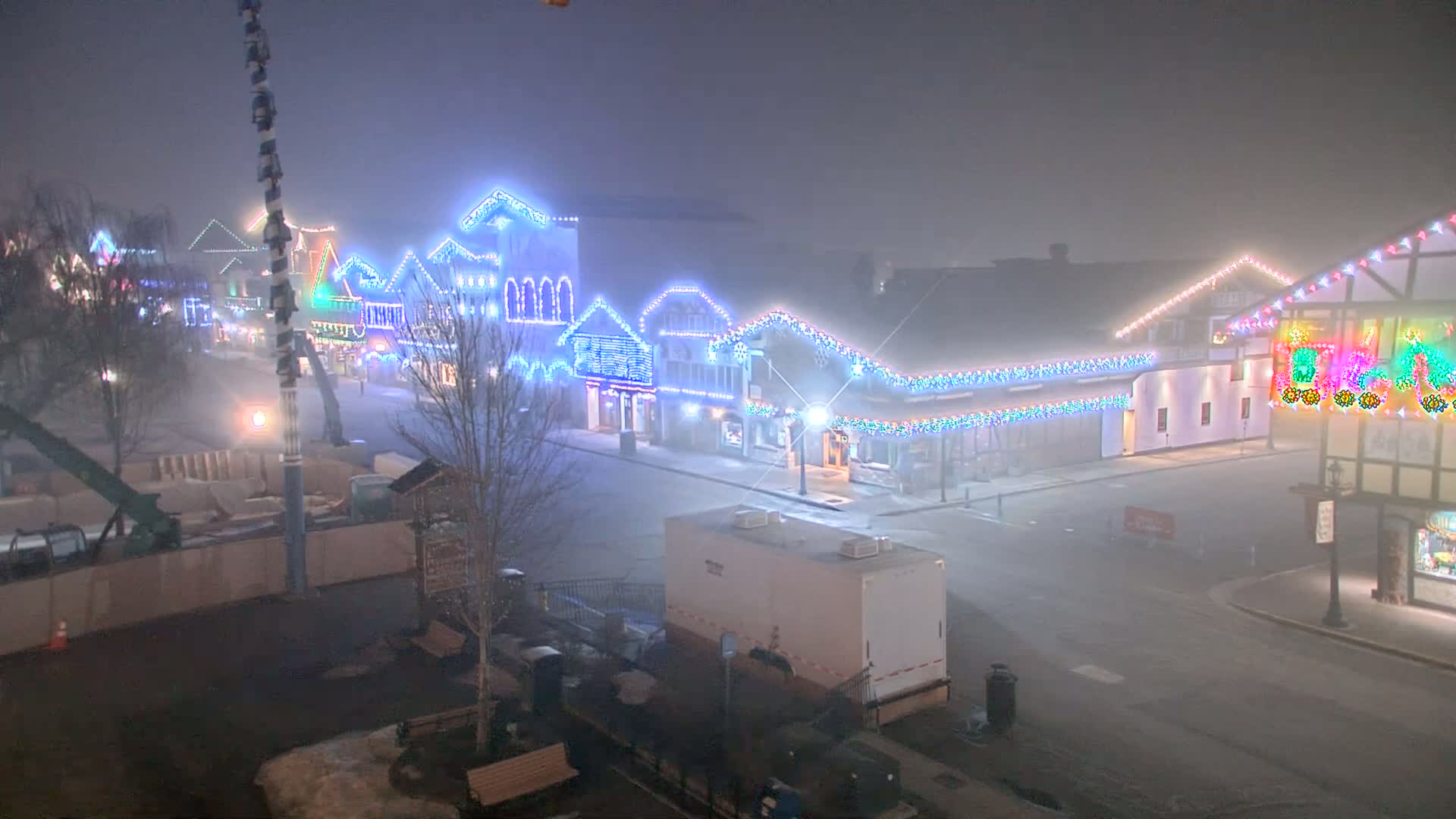 A fog-shrouded street at night, lined with buildings decorated with colorful Christmas lights.