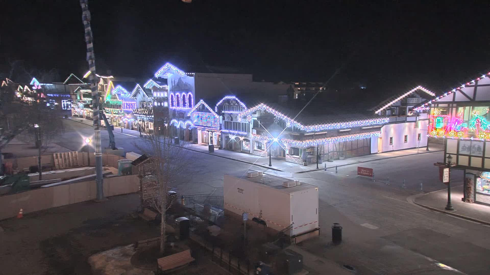 A mostly empty street at night lined with festively lit buildings, under a clear, dark sky.