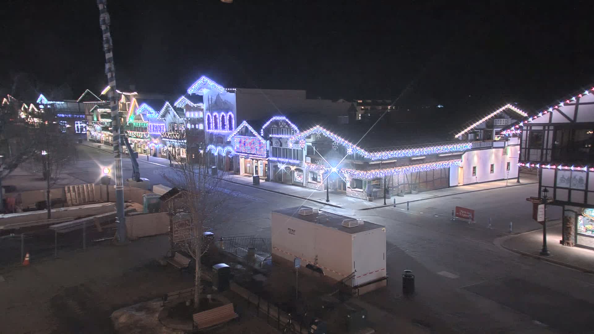 A mostly empty street at night lined with festively decorated buildings, brightly lit with Christmas lights.