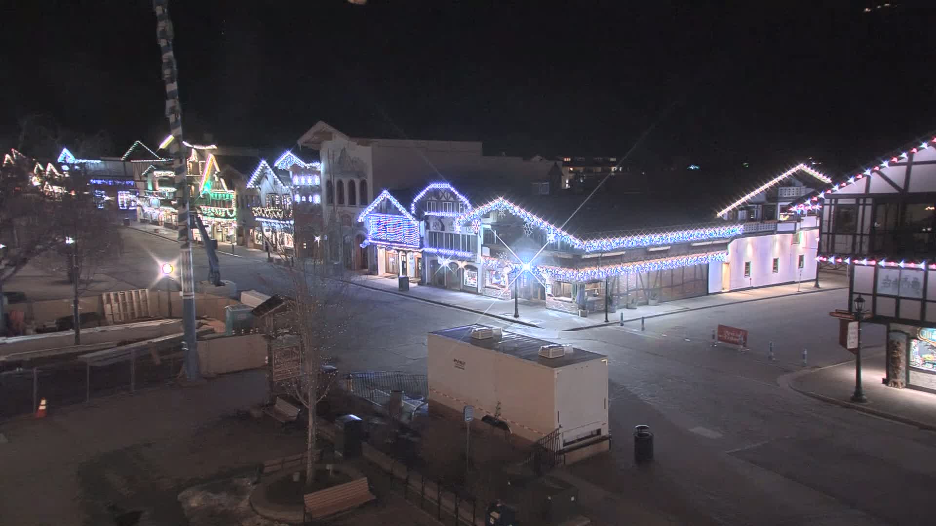 A nighttime, empty street lined with festively lit buildings.