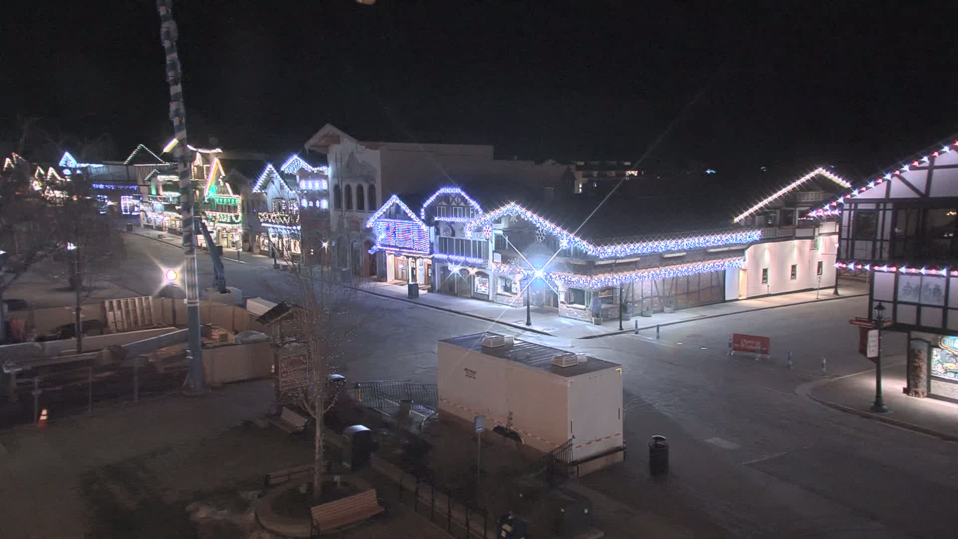 A nighttime, snow-covered street lined with festively decorated buildings, some under construction.