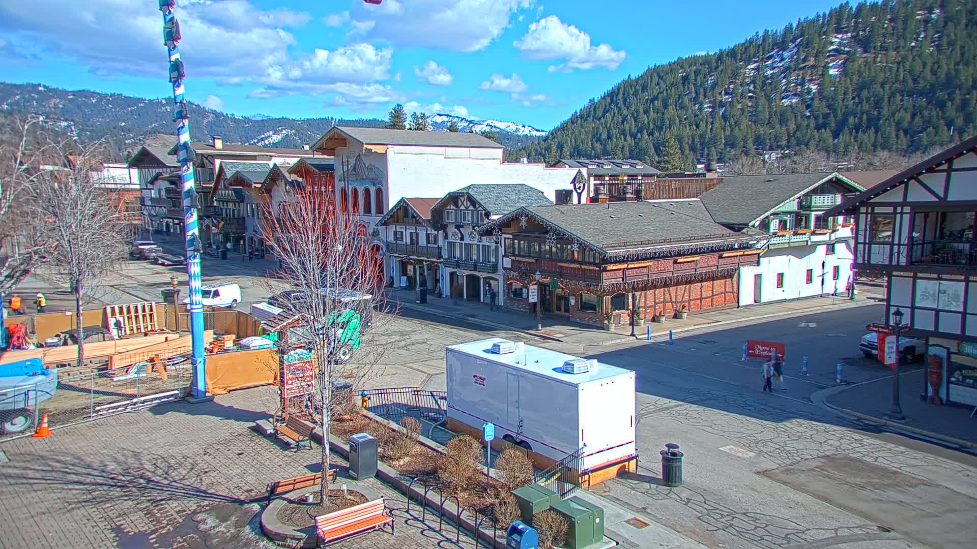 A town square with several buildings in a Bavarian style, under a partly sunny sky, is partially under construction.