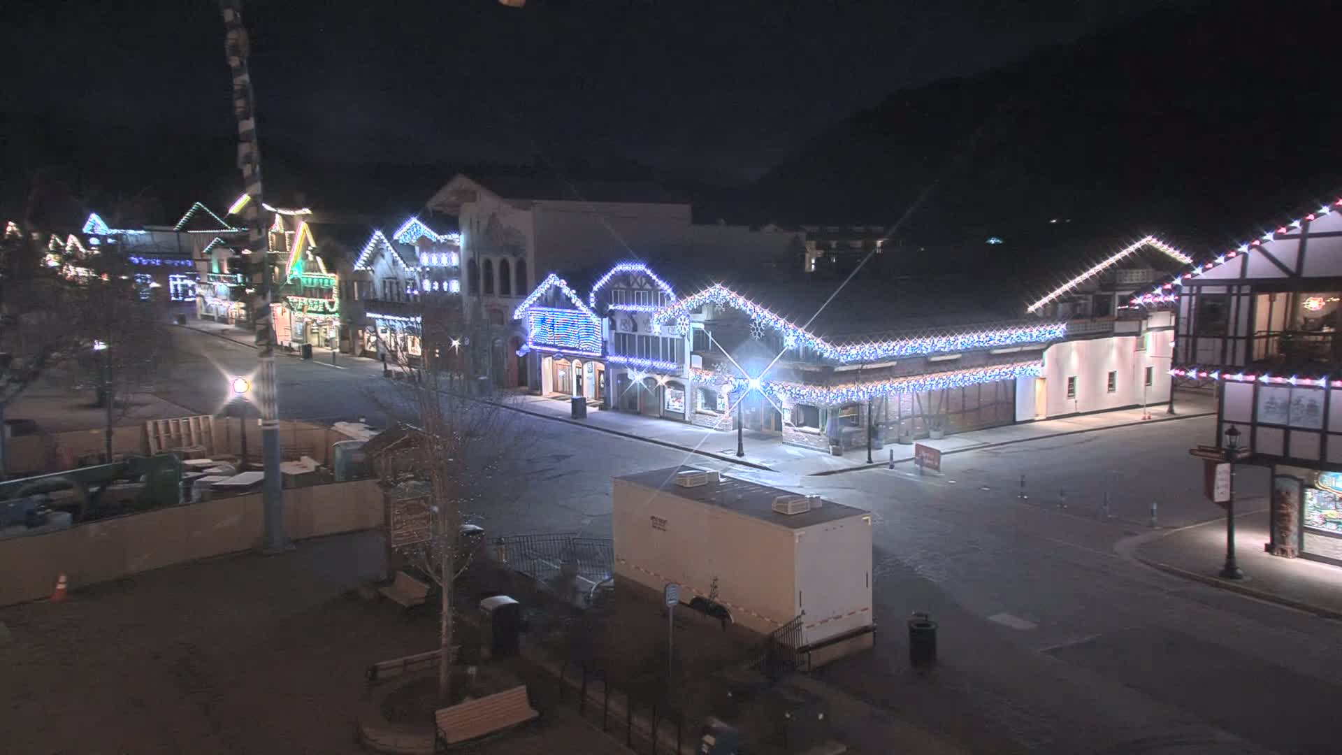 A mostly empty street at night lined with buildings decorated with twinkling lights.