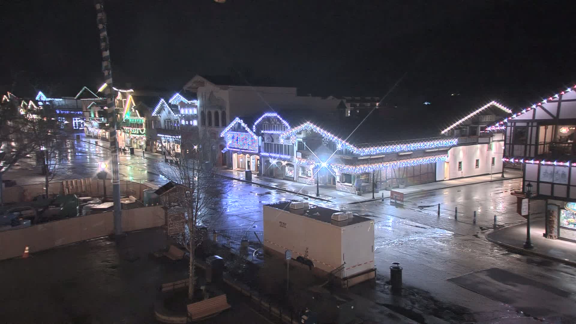 A rain-slicked street at night lined with buildings decorated with Christmas lights.