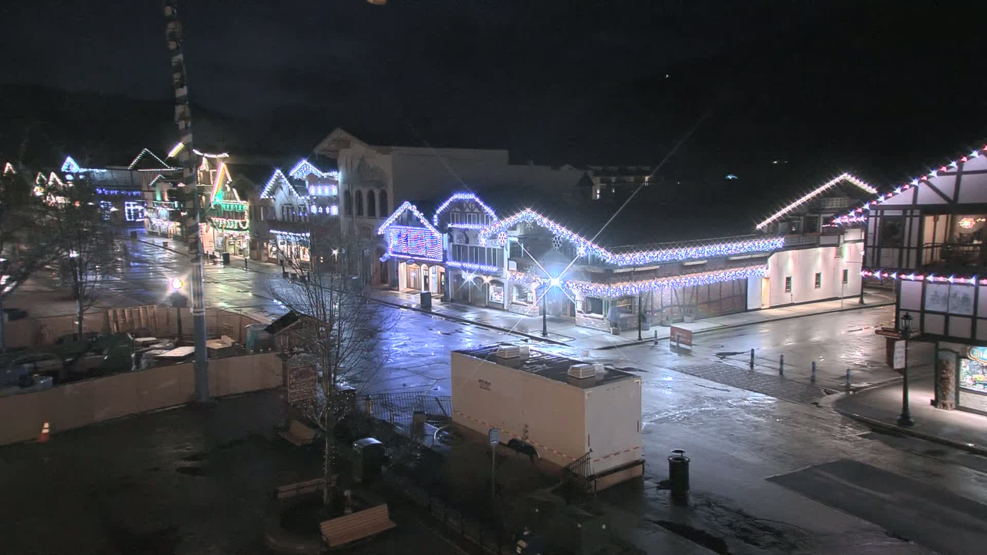 A wet, empty street at night lined with festively lit buildings.
