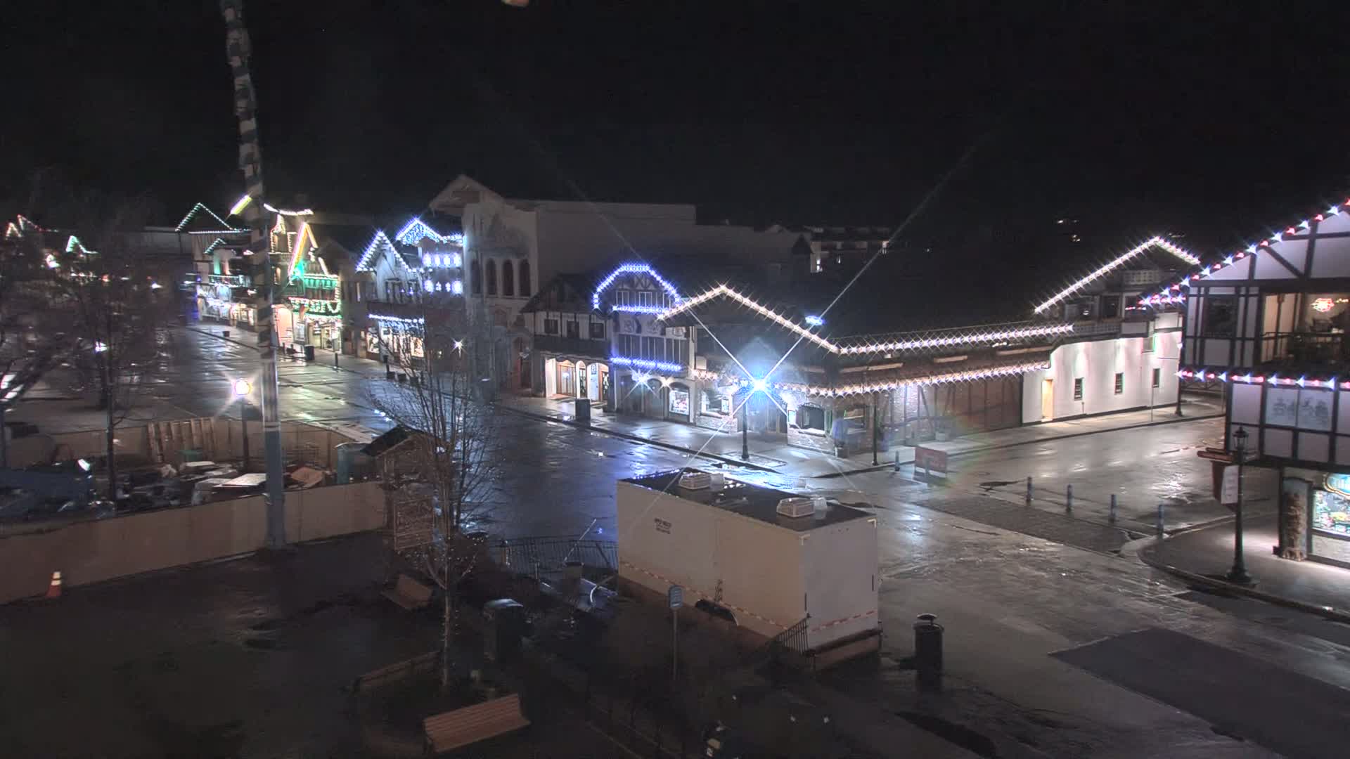 A wet, empty street at night lined with festively lit buildings.