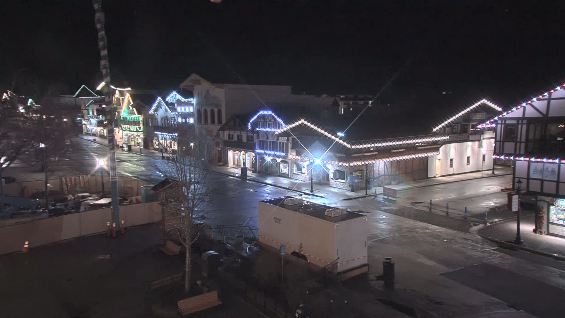 A mostly empty, wet street at night lined with festively-lit buildings.