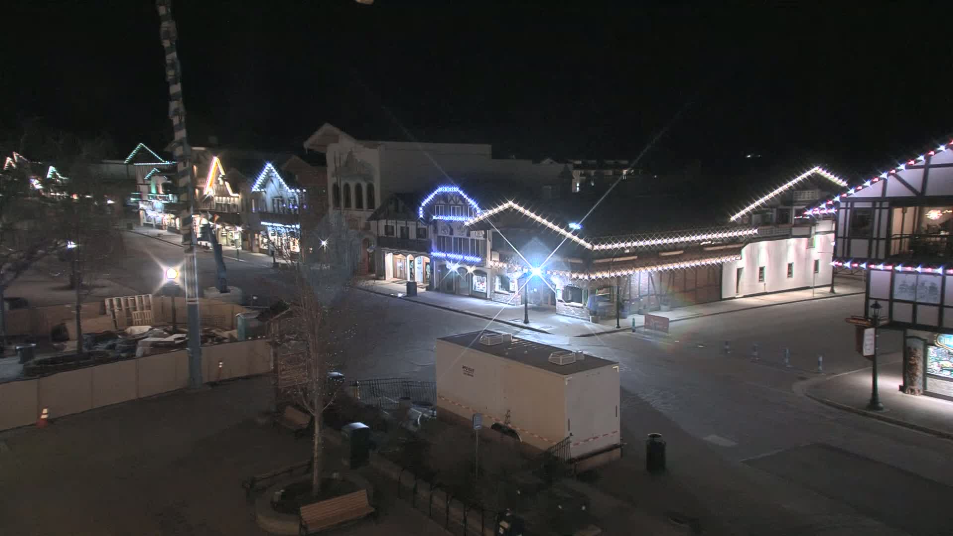 A mostly empty street at night lined with festively lit buildings, under a clear sky.