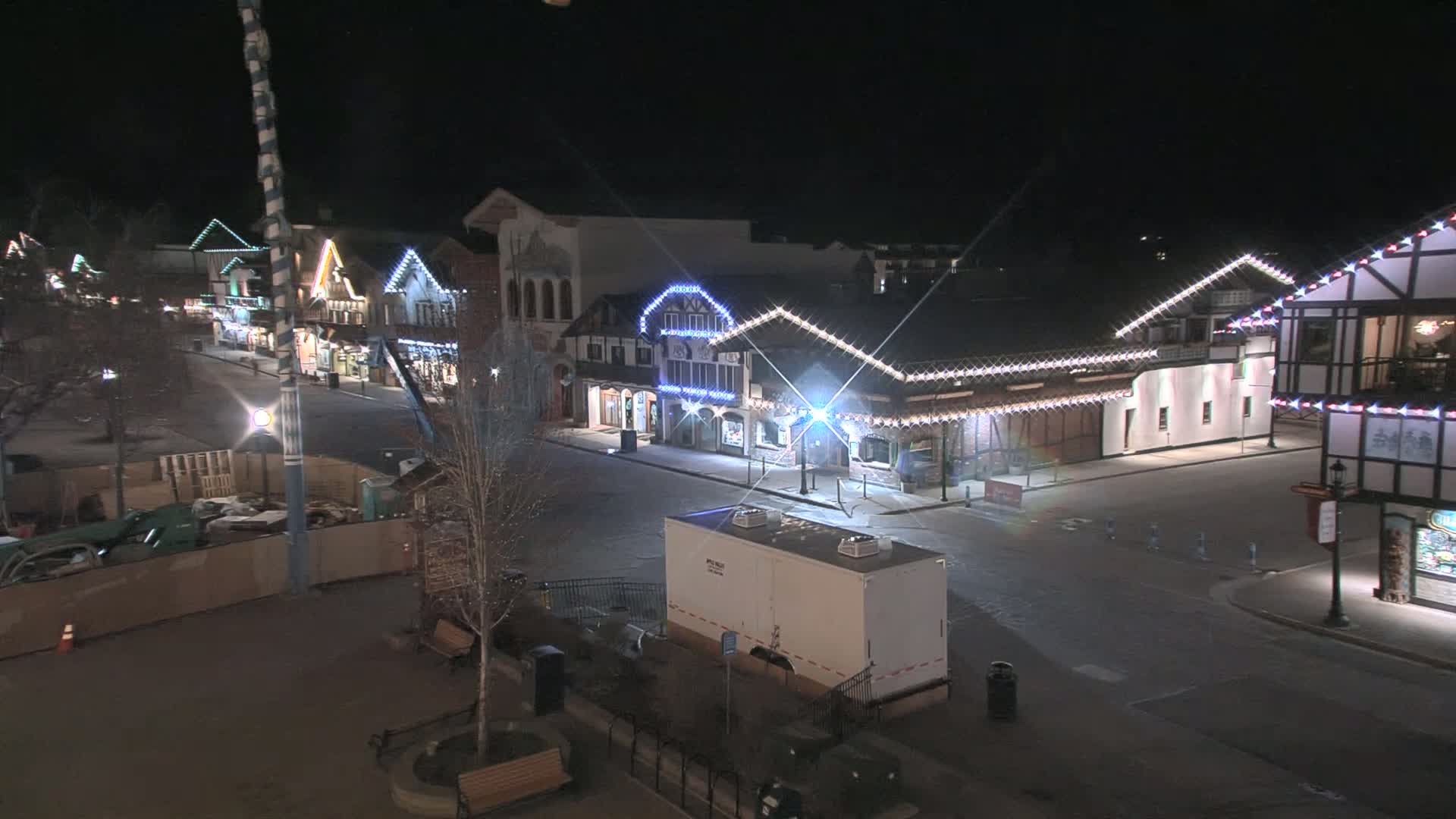 A mostly empty, illuminated street at night lined with European-style buildings, featuring construction in the foreground.