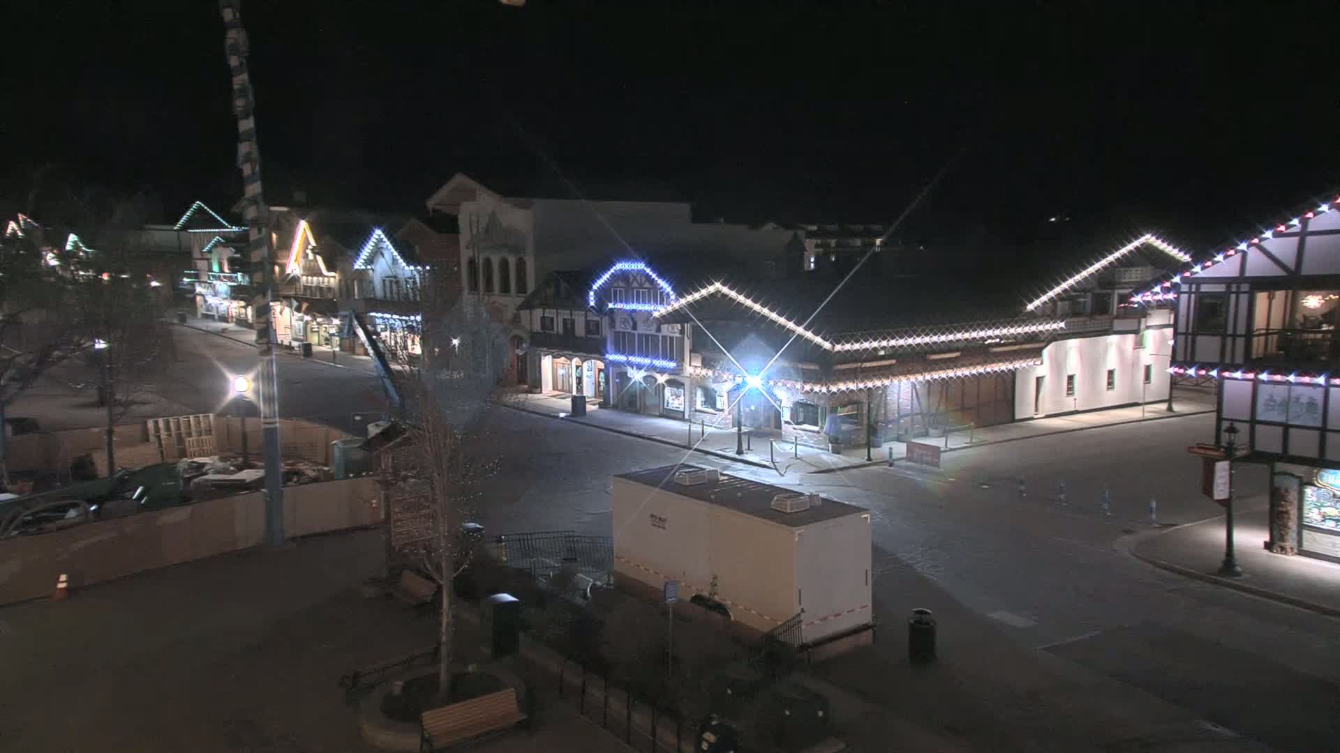 A nighttime, street-level view of a row of illuminated buildings, possibly in a village or town square, under a clear, dark sky.