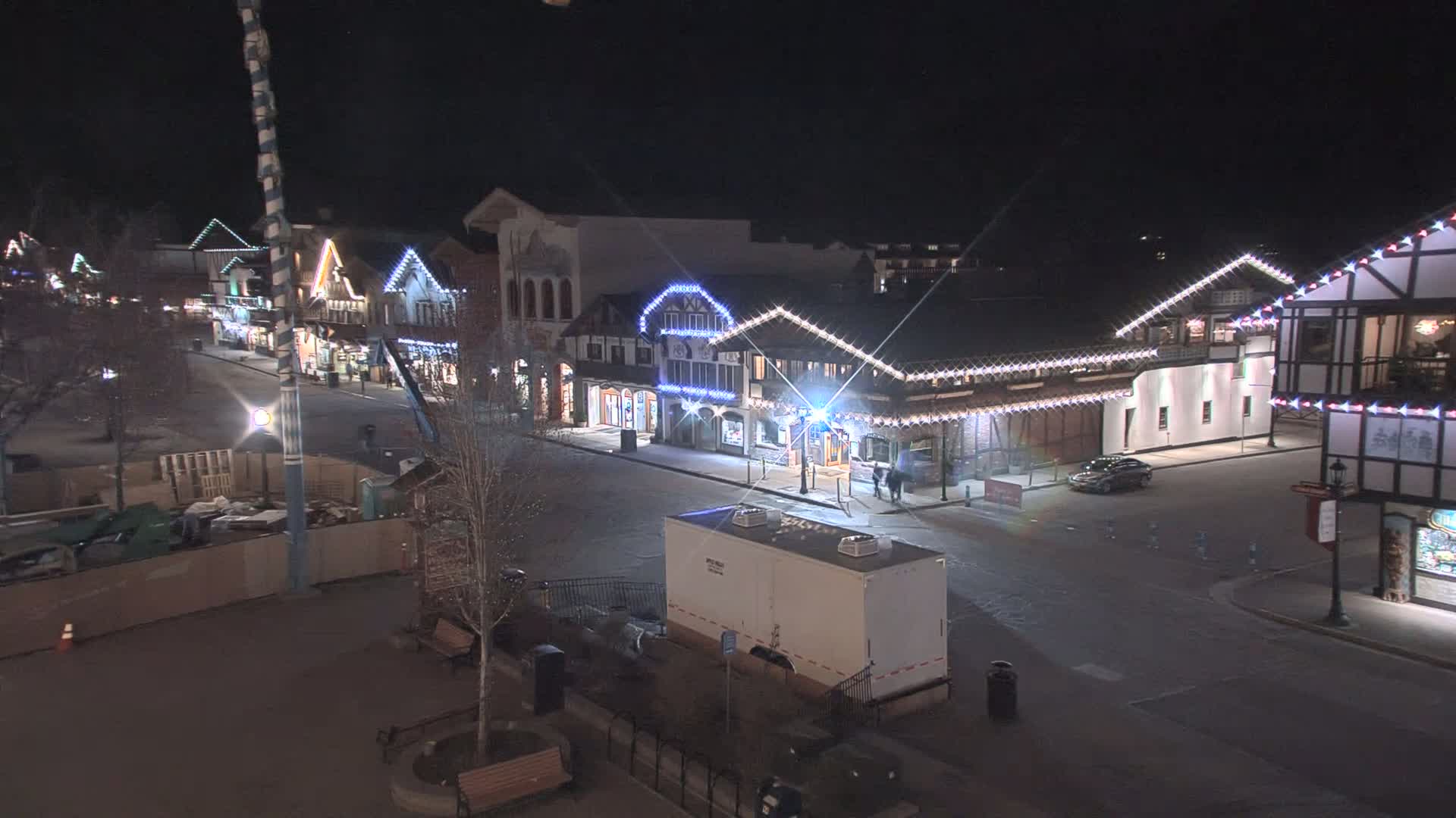A snow-dusted street at night lined with illuminated buildings decorated with Christmas lights.