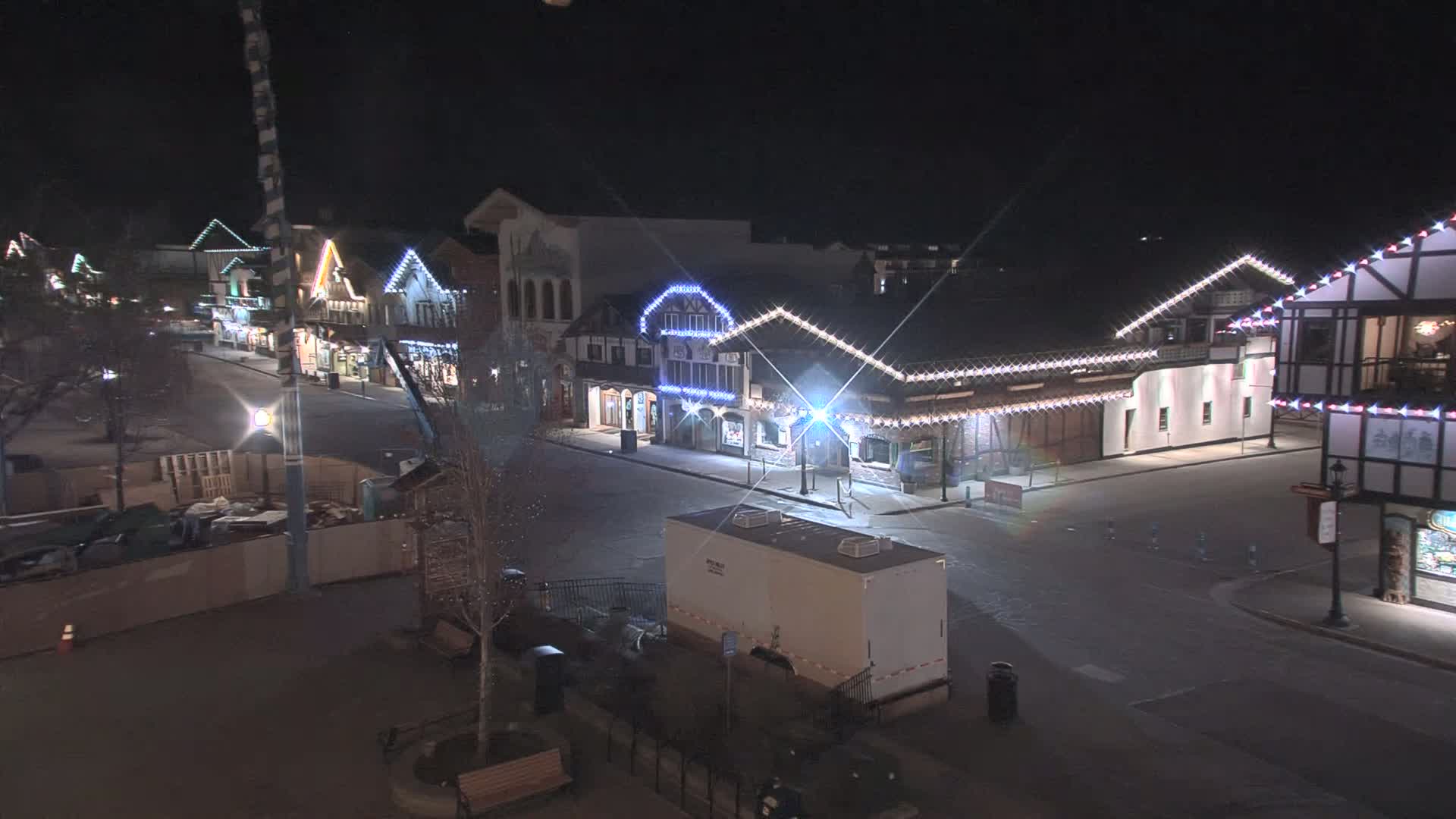 A mostly empty street at night lined with festively lit buildings, under clear skies.