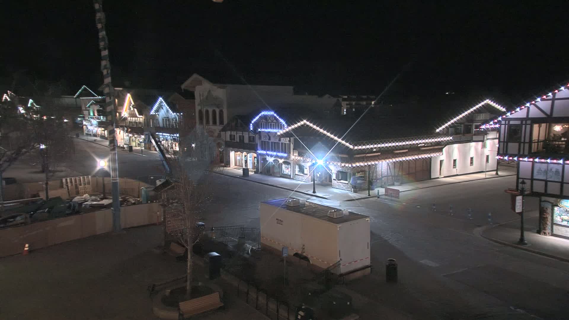 A mostly empty street at night lined with festively lit buildings, under clear skies.