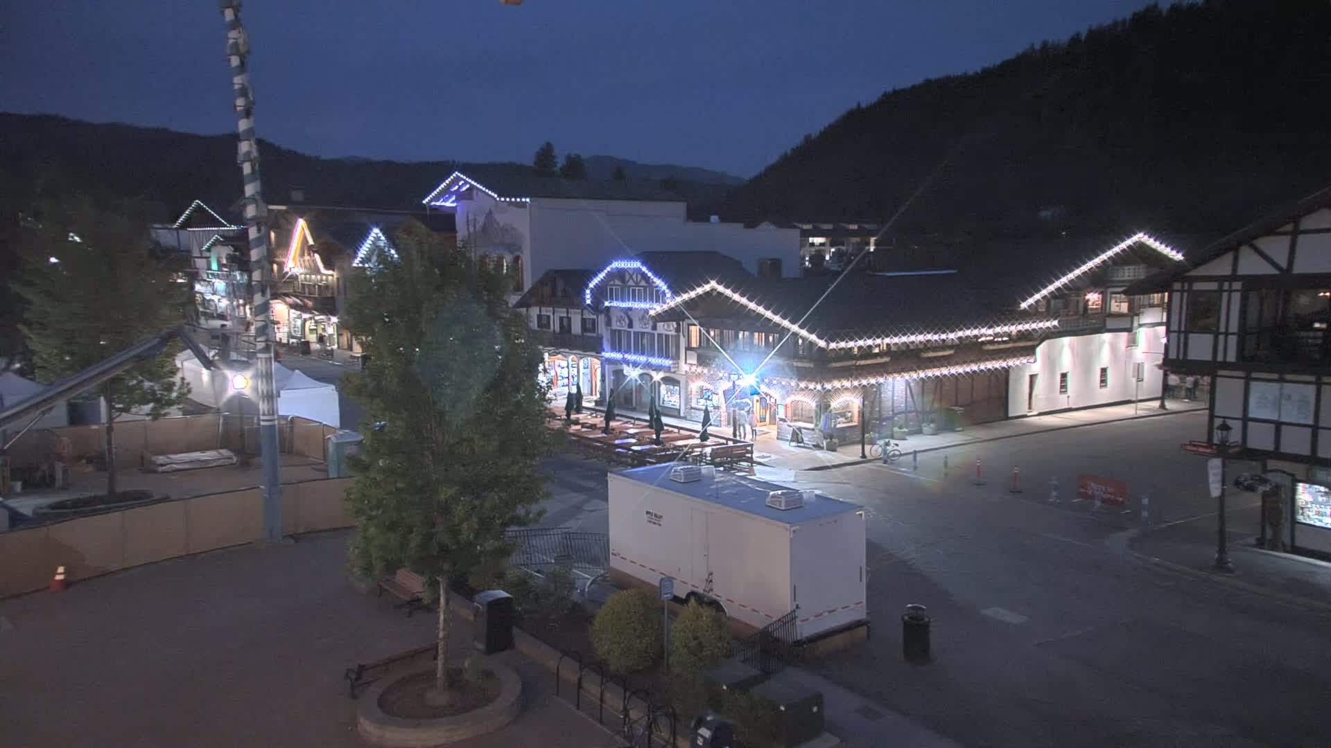 A nighttime view of a town square with several buildings decorated with string lights, under a dark sky.