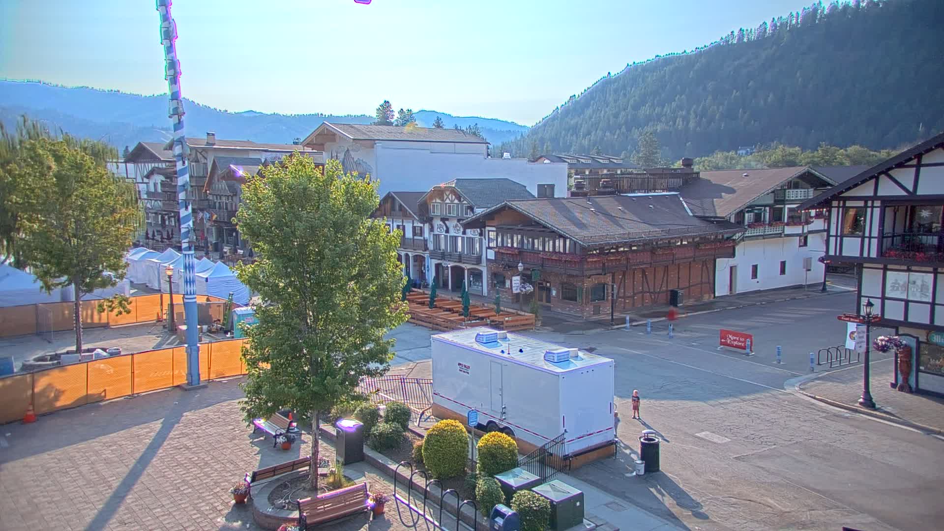A town square with Bavarian-style buildings, surrounded by mountains under a clear, sunny sky.