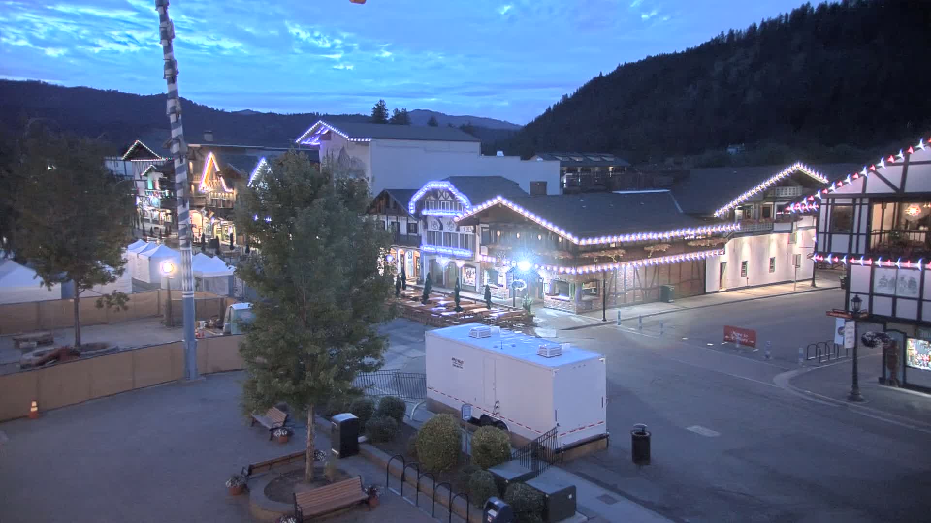 A town square with Bavarian-style buildings illuminated at dusk under a mostly clear sky.