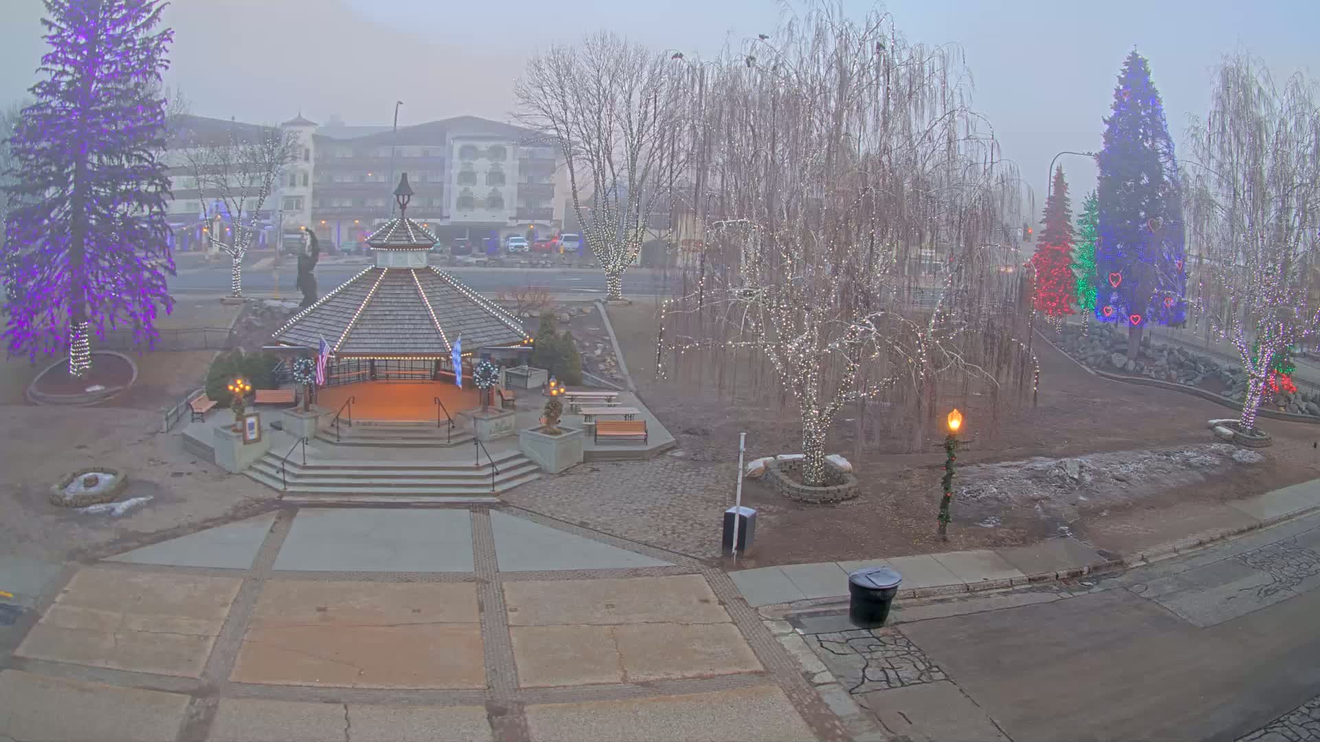 A gazebo, several decorated trees, and a building are visible in a foggy town square.