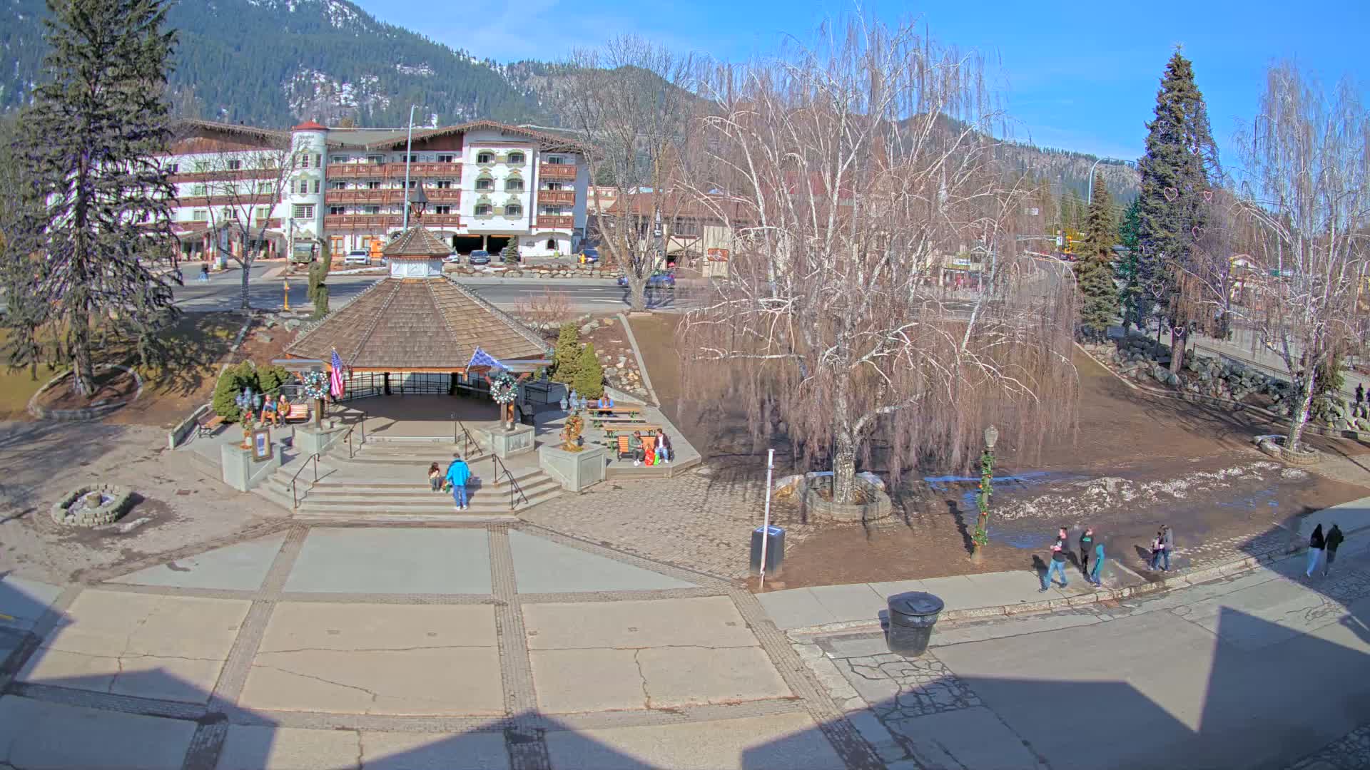 A town square with a gazebo, a few people walking around, and bare trees under a sunny sky.