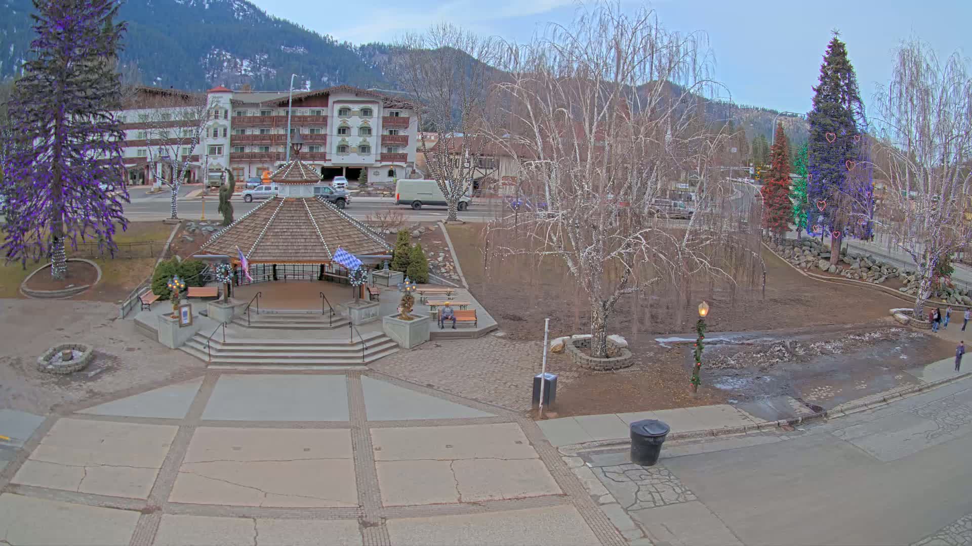 A town square with a gazebo, decorated trees, and a hotel in the background on a partly cloudy day.