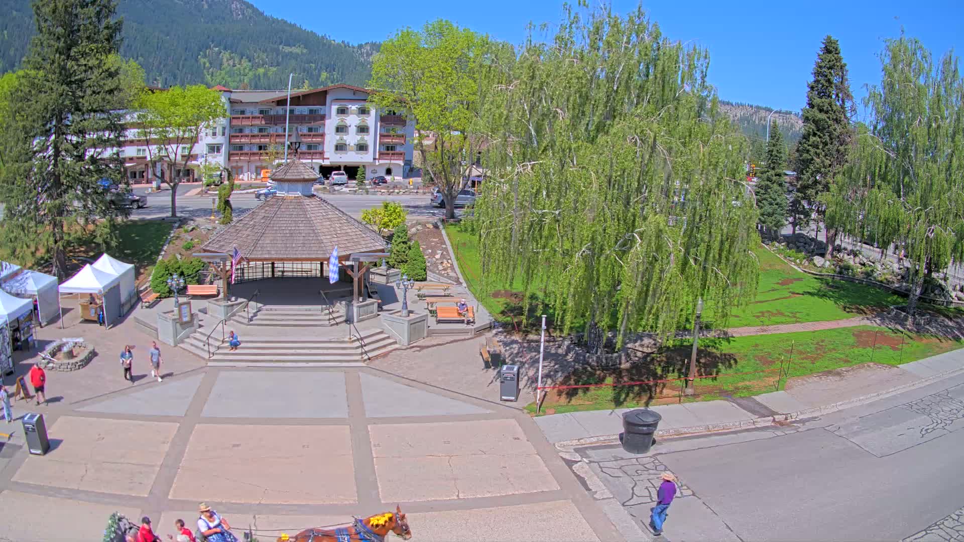 A town square with a gazebo, a multi-story building in the background, and a horse-drawn carriage, all under a sunny sky.