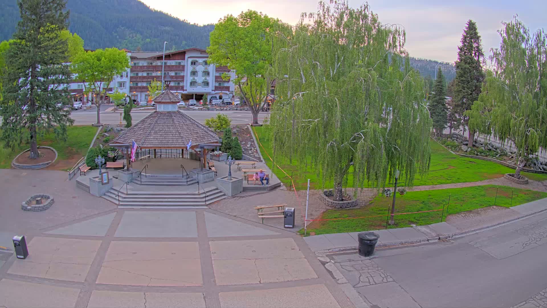 A gazebo sits in a town square next to a multi-story building under a partly cloudy evening sky.