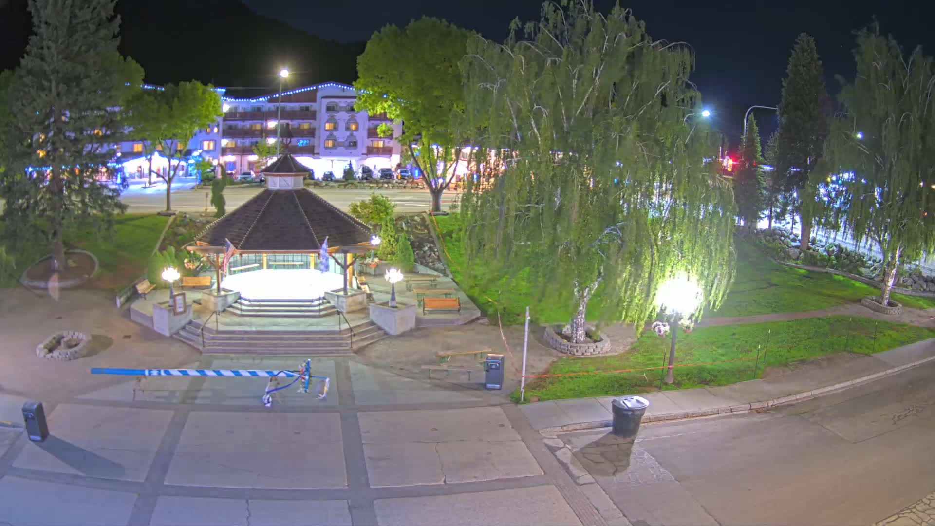 A nighttime view of a town square with a gazebo, trees, and a building in the background.