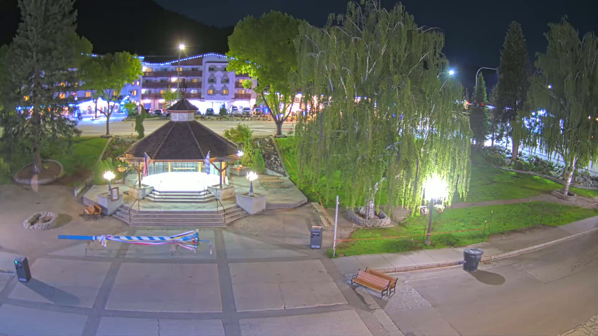 At night, a town square with a gazebo, trees, and a building with lights is illuminated.