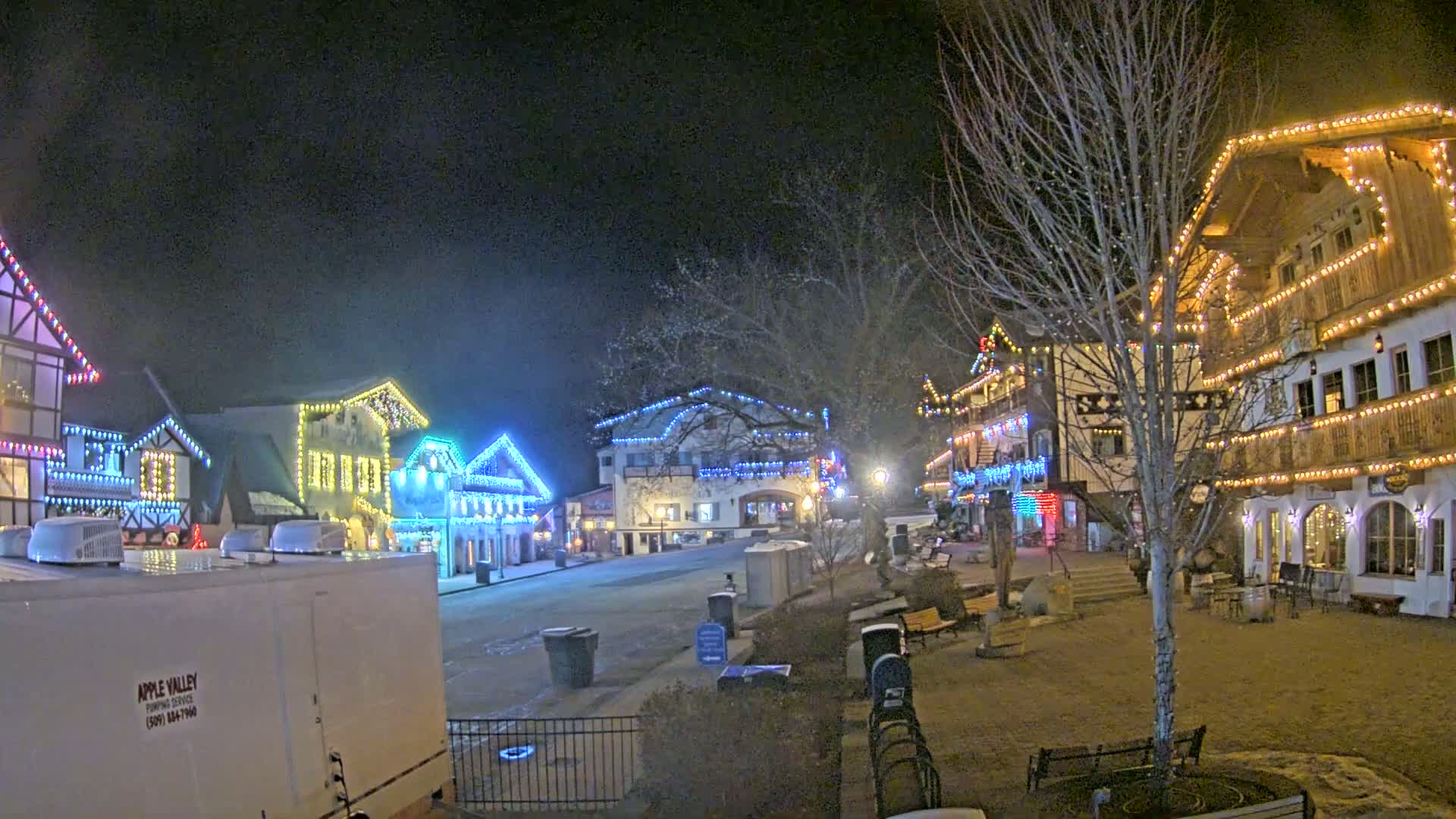 A nighttime scene of a village square with several buildings decorated with colorful Christmas lights.