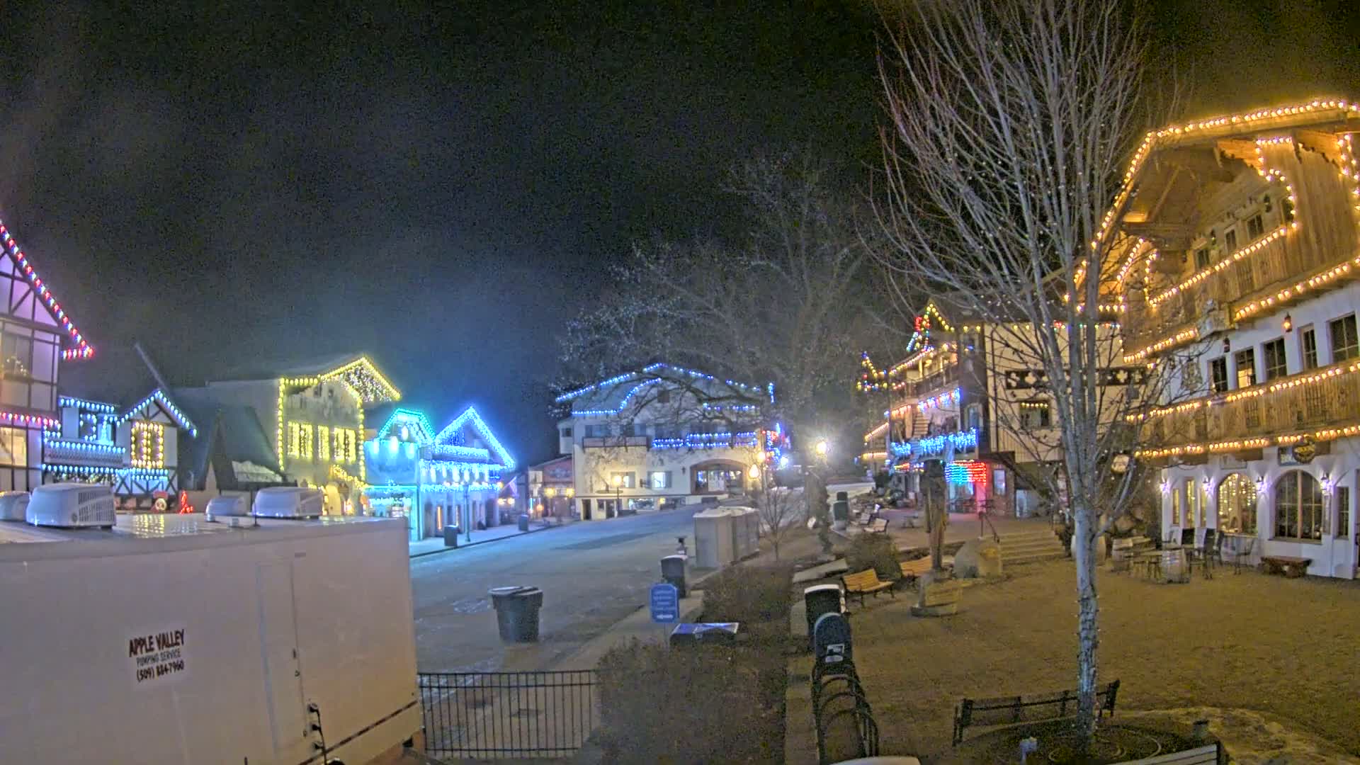 A nighttime scene of a town square with several buildings decorated with colorful lights.