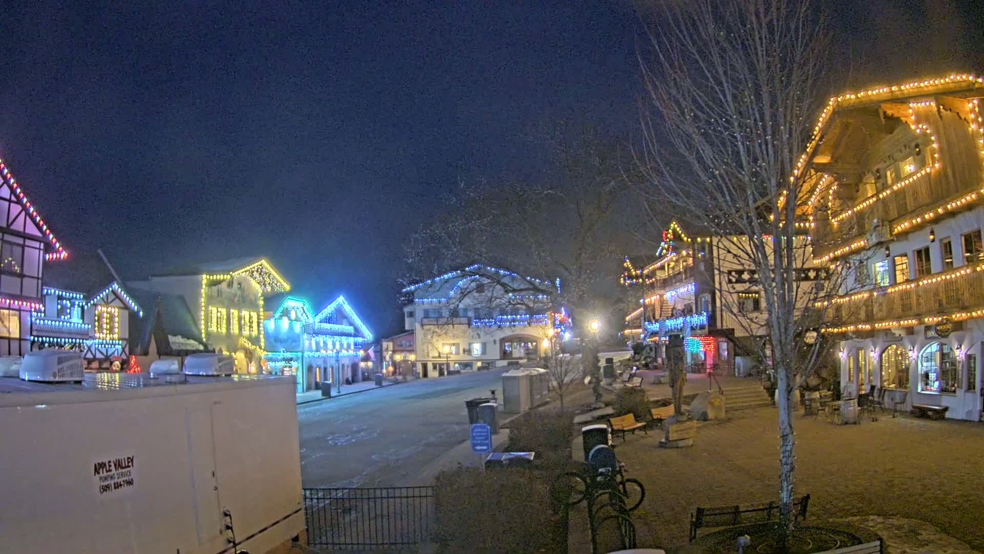 Several buildings decorated with colorful Christmas lights line a quiet, snow-dusted street at night.
