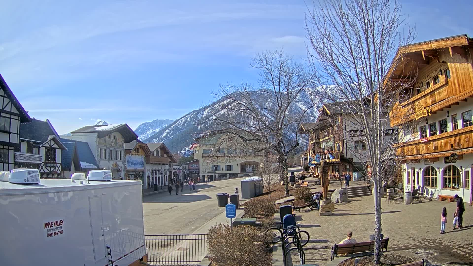 A sunny day reveals a quaint village nestled in a valley, with snow-capped mountains in the background.