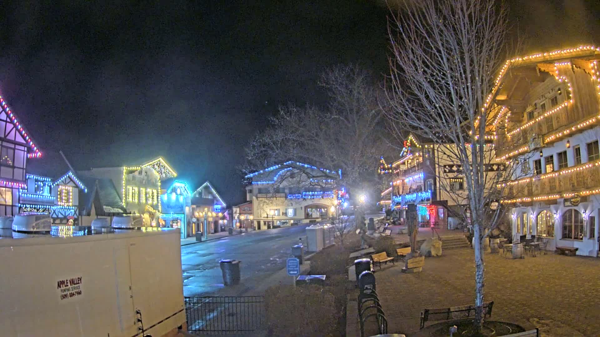 A nighttime scene of a town square with several buildings decorated with colorful lights, under a clear, dark sky.