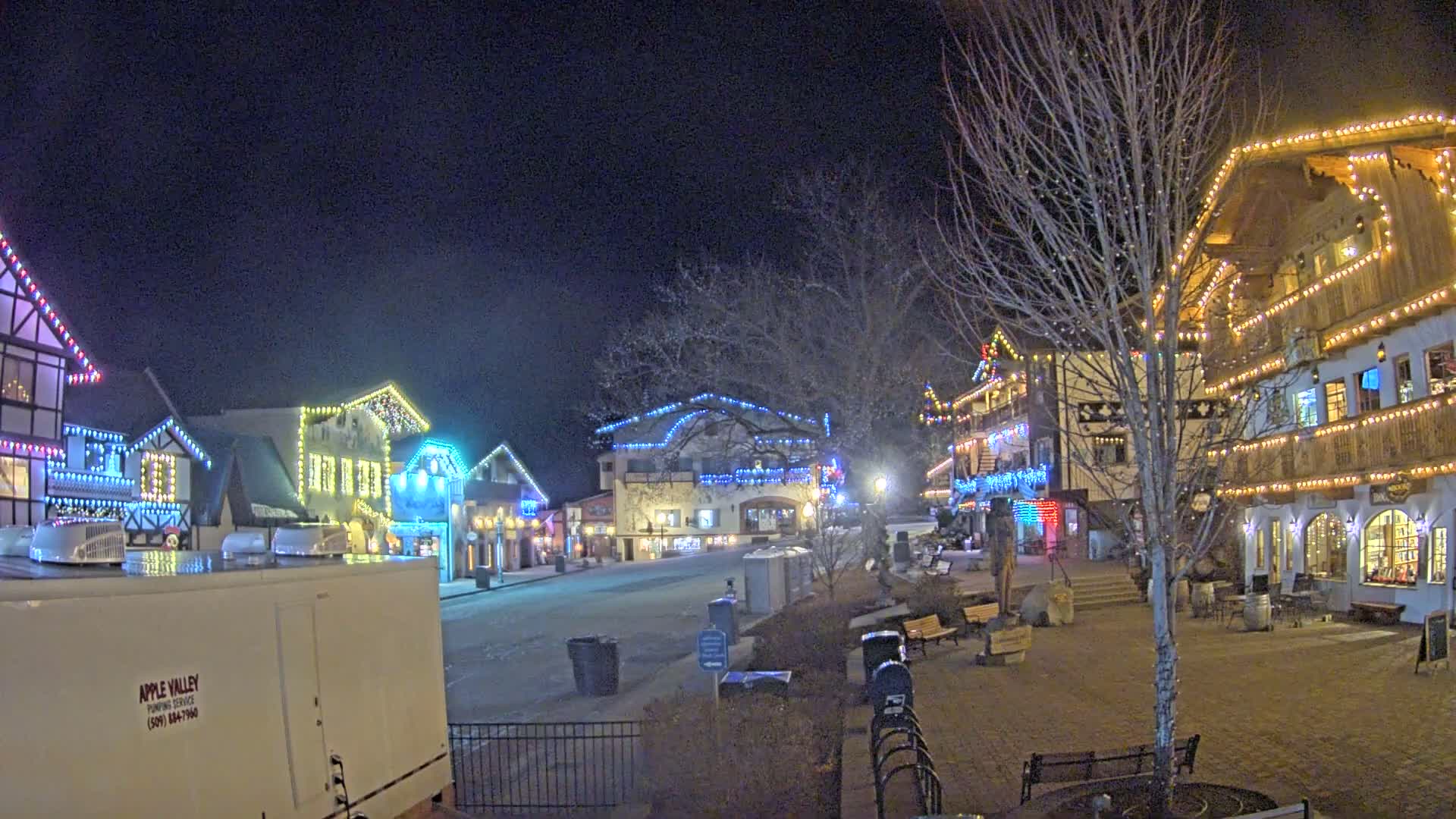 A nighttime scene of a town square with several buildings decorated with colorful Christmas lights.