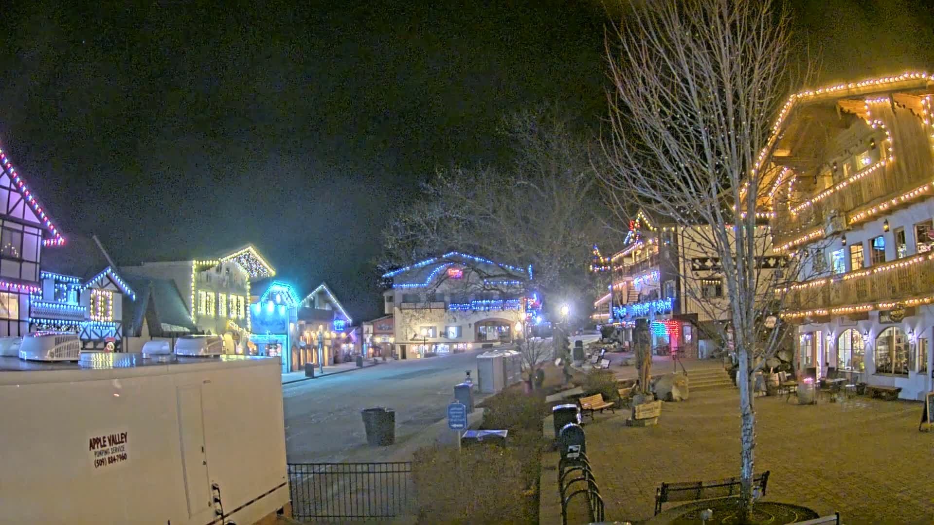 A nighttime scene of a town square with several buildings decorated with colorful lights, under a clear, dark sky.