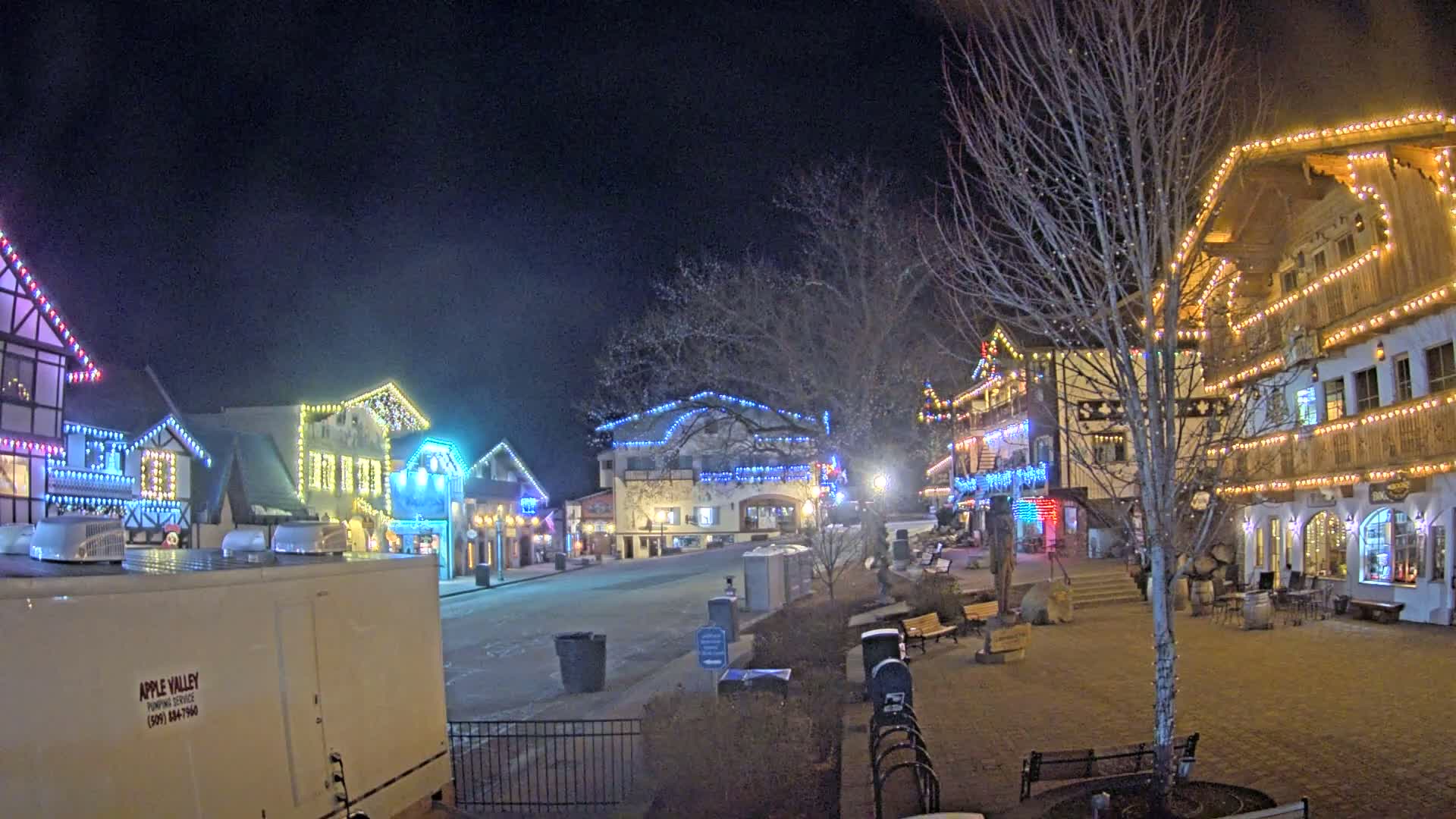 A nighttime view of a town square with several buildings decorated with colorful Christmas lights.