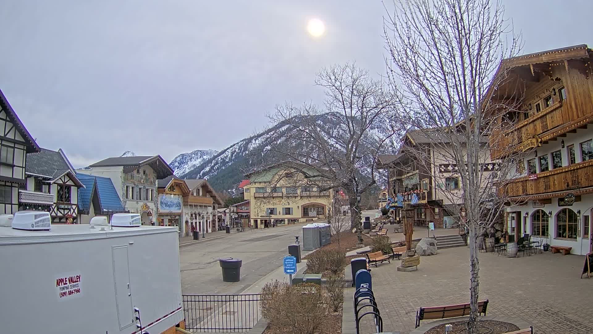 A mostly sunny day reveals a quaint, European-style village nestled against snow-capped mountains.